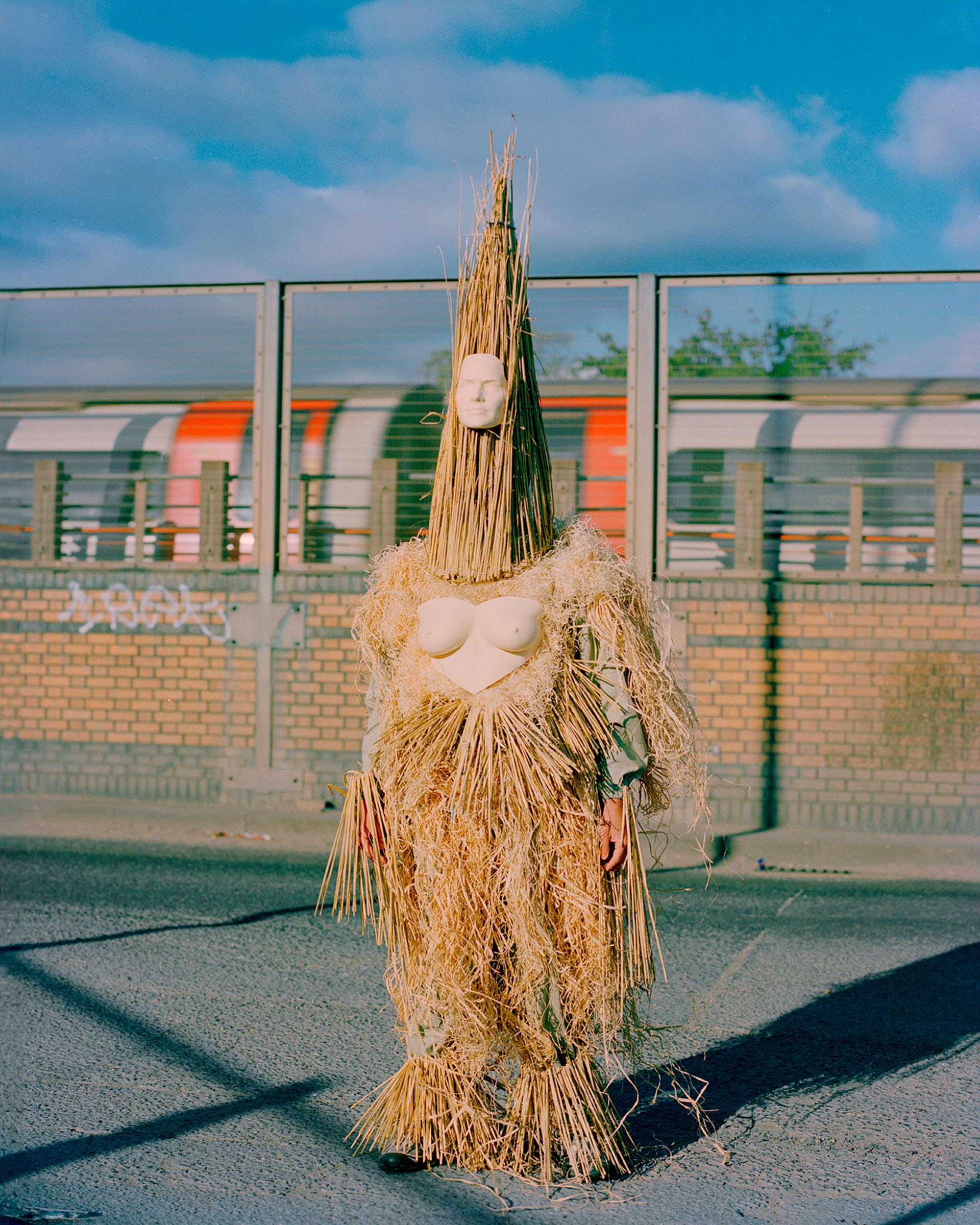 A lone figure of straw and masquerade standing in an urban landscape