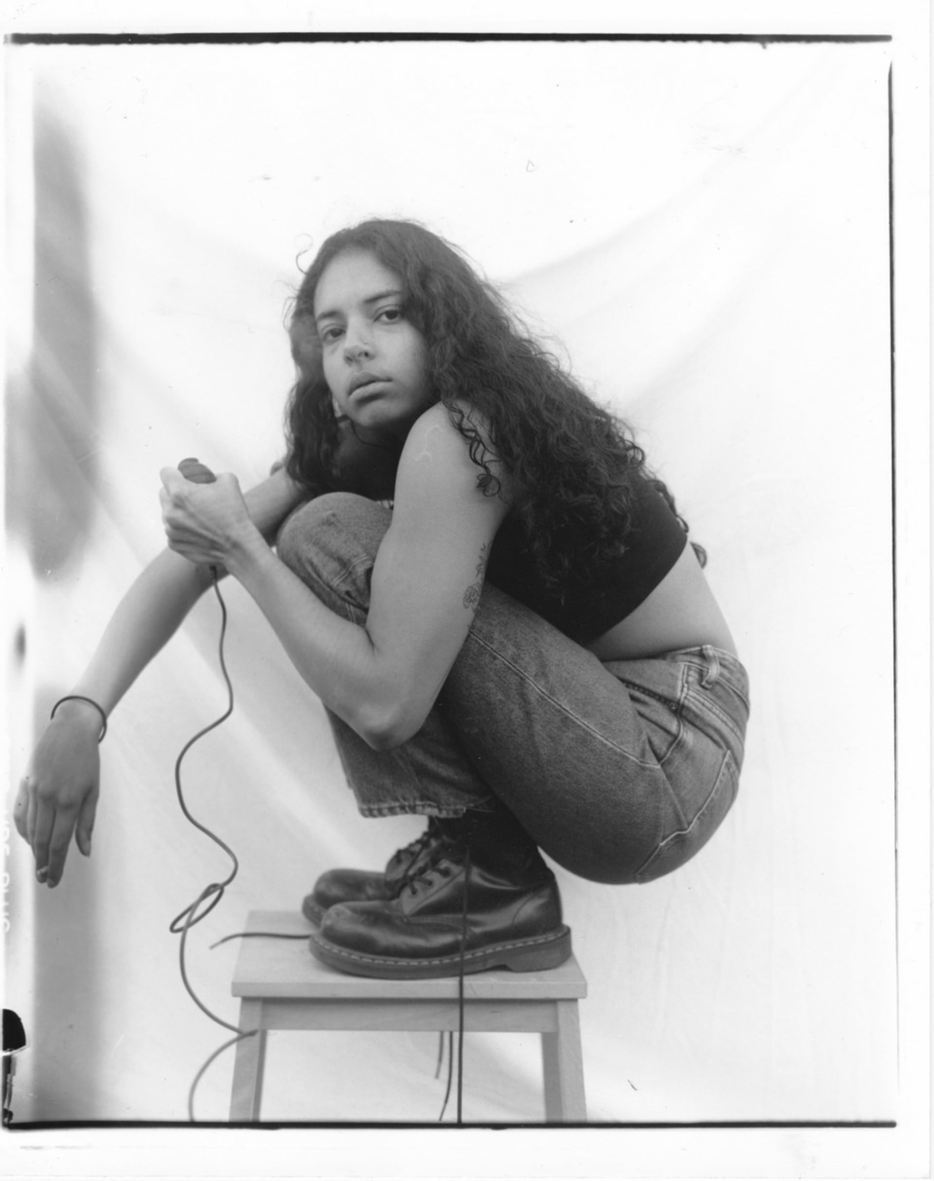 black and white self-portrait, crouched down on wooden steps, facing the camera side on, holding a cigarette