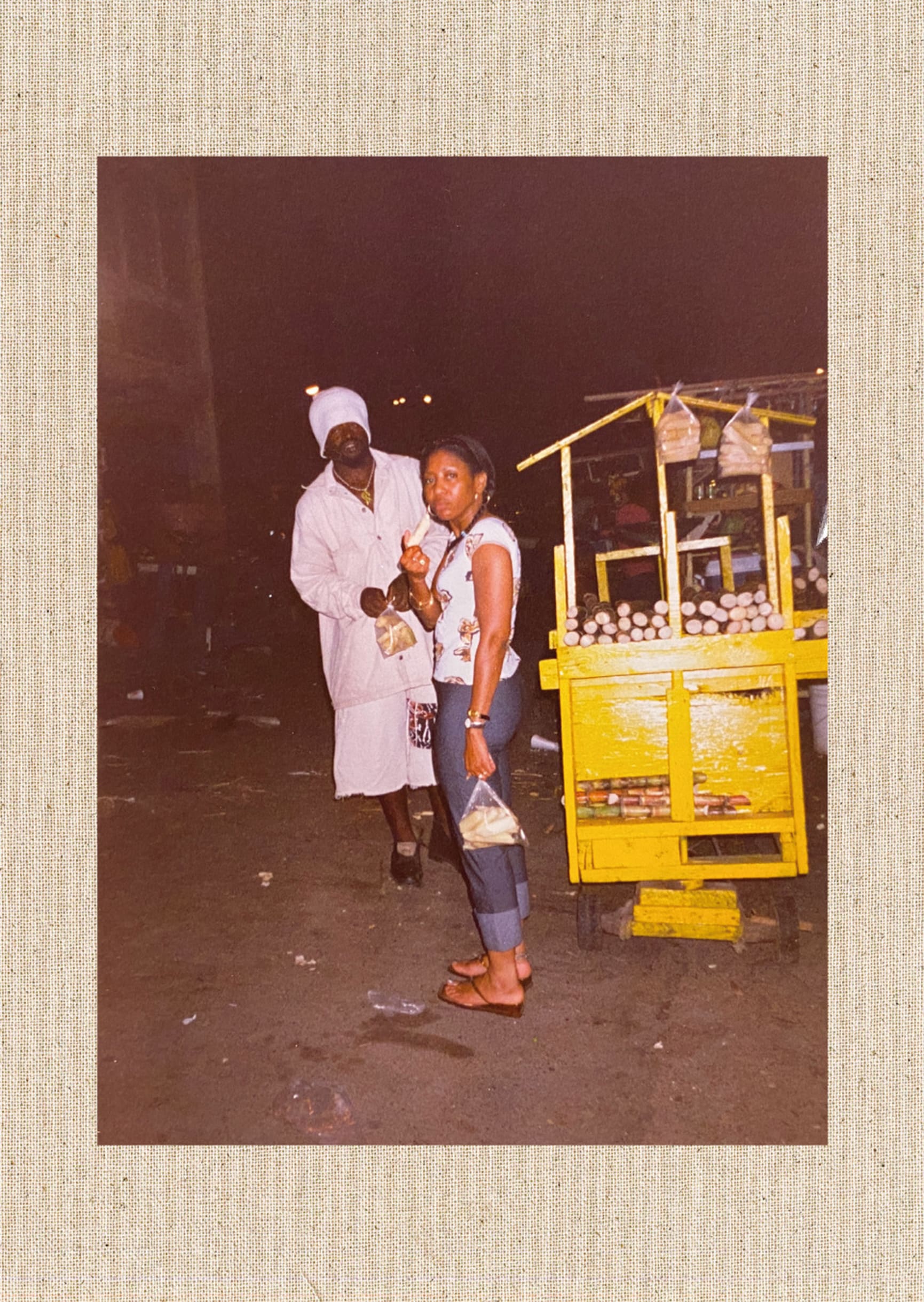 Photograph of my mother in Jamaica chewing sugar cane, next to a cane seller with a yellow stall.