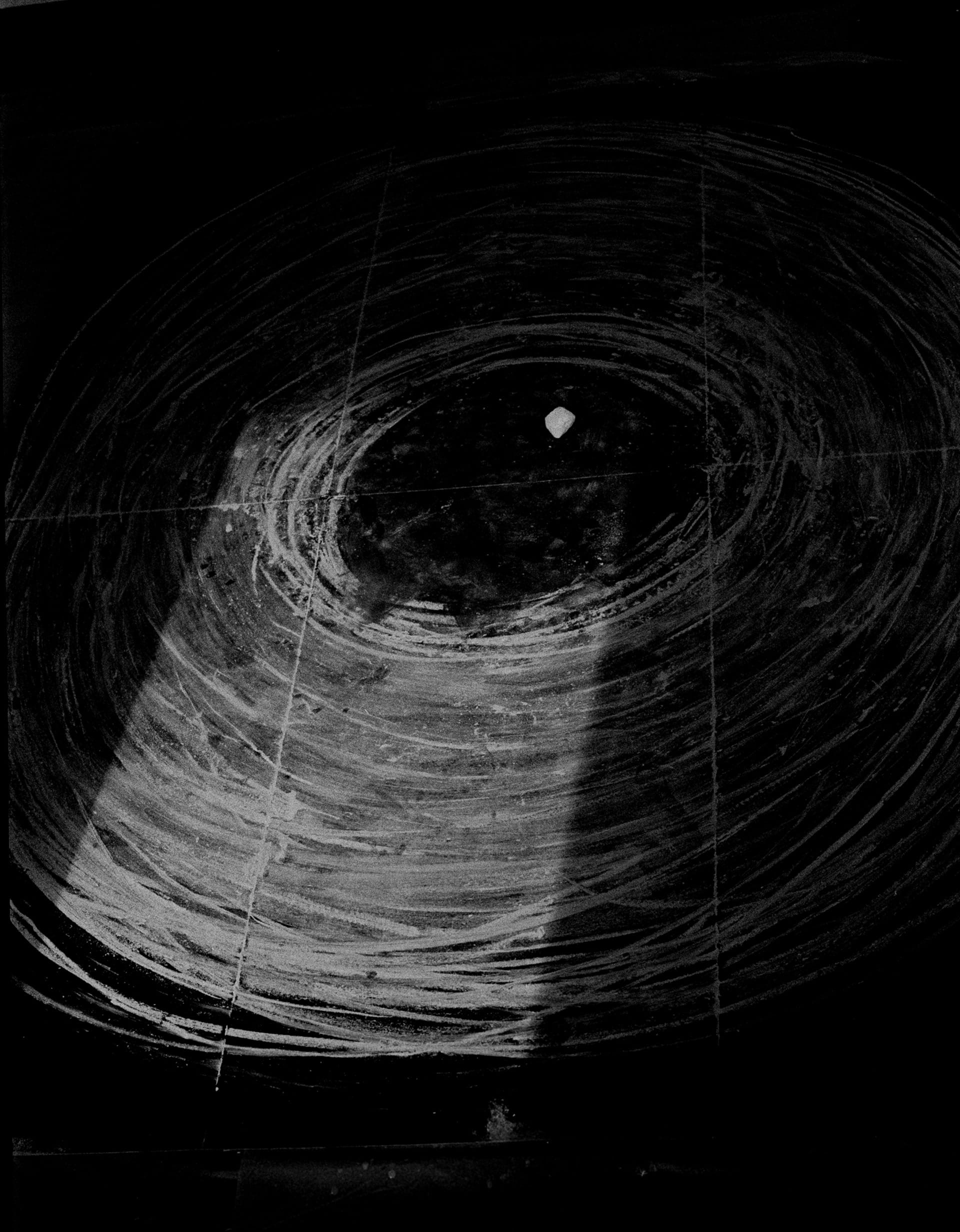 high contrast image showing a section of a circular drawing made with chalk on a black board. 