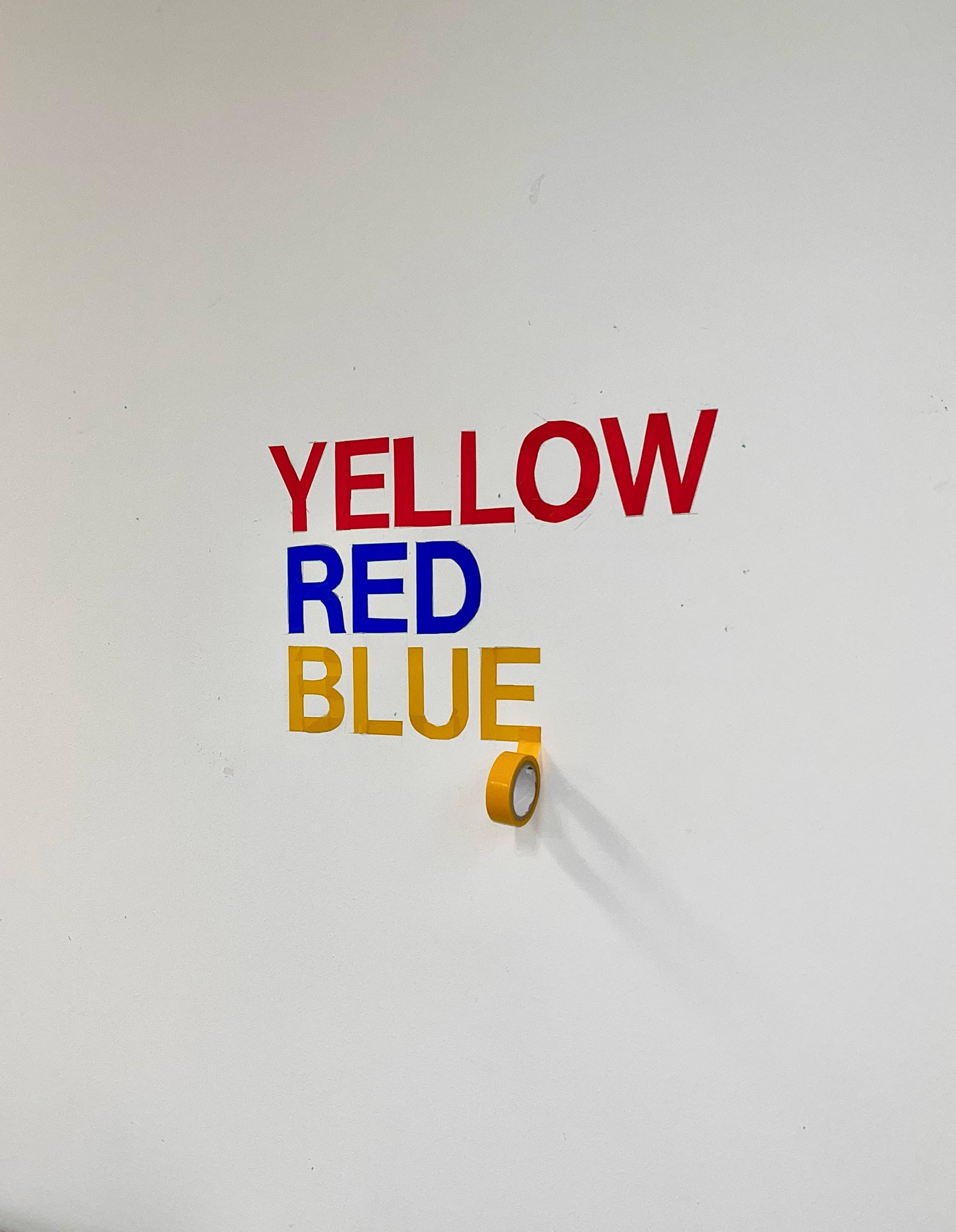 Words Yellow, Red and Blue written in the wall with coloured tape. 