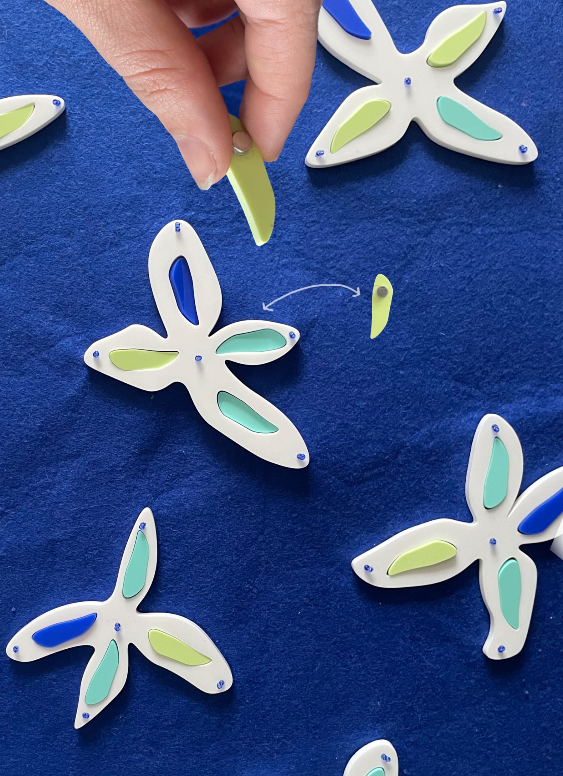 Blue felt with plastic flowers sewn in. Elements of the petals can attach in through the use of a magnet for colour choice.