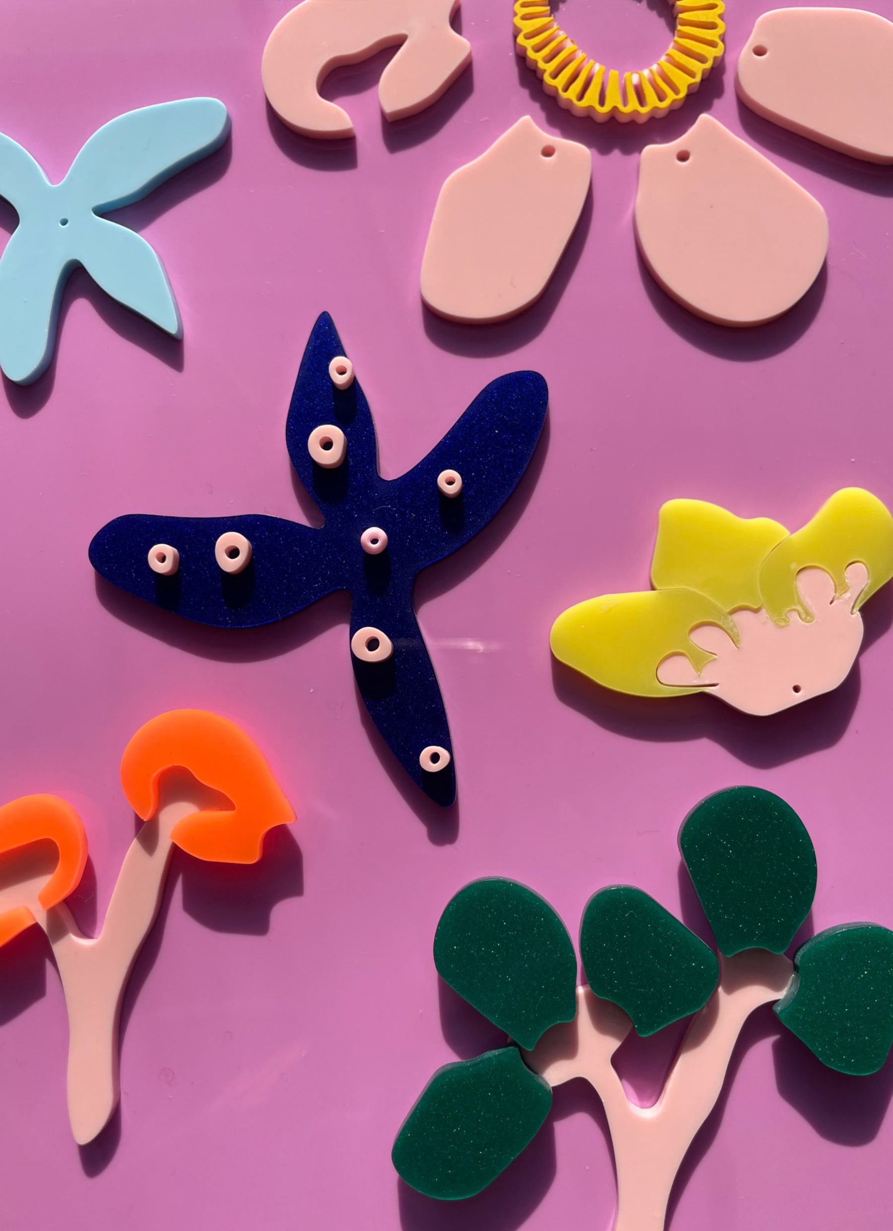 Various abstract flower motifs made of plastic varying in colours are placed into a composition on a purple plastic background.