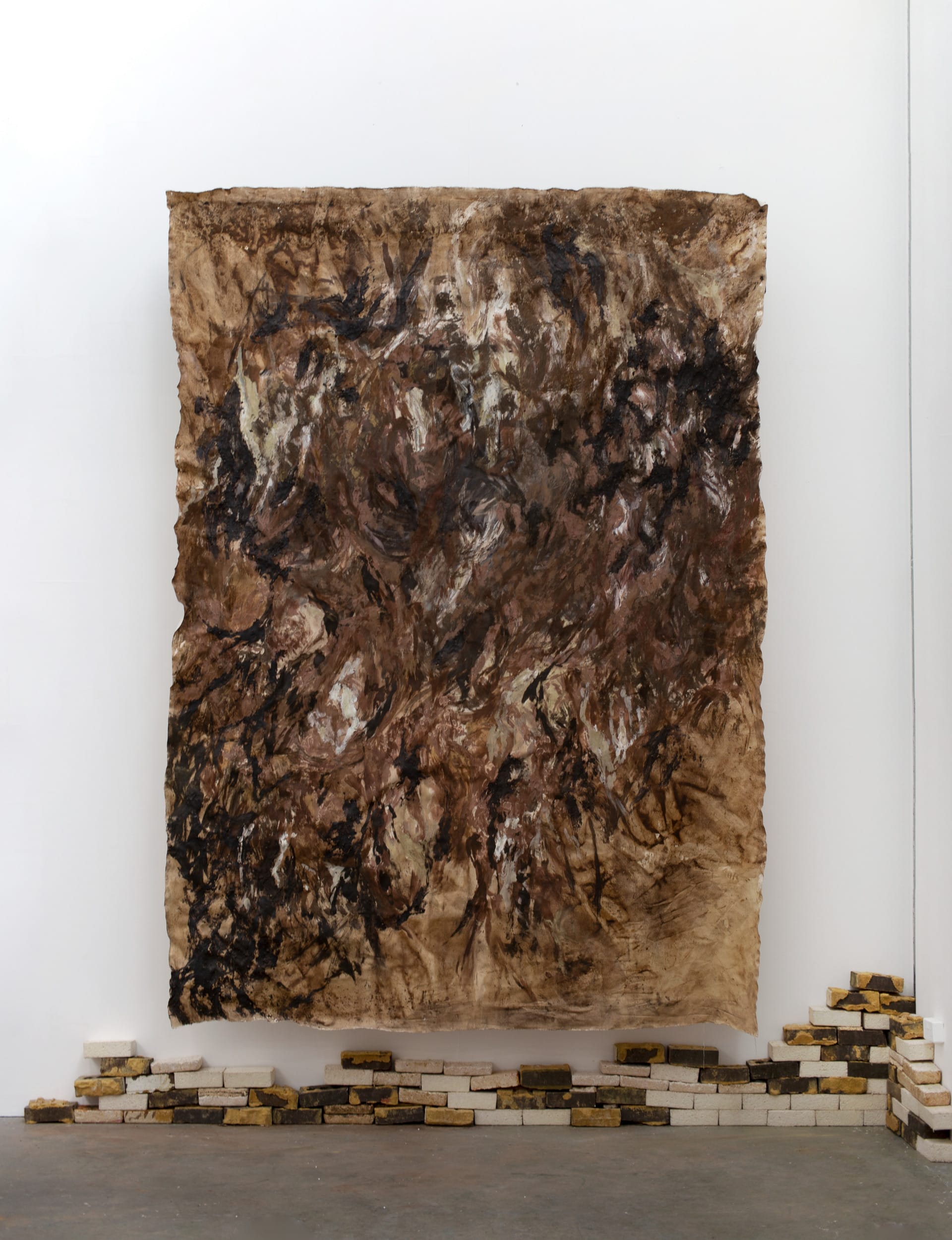 Large, 4 meter brown, abstract painting hung above a short decaying wall of bricks and mycelial composites