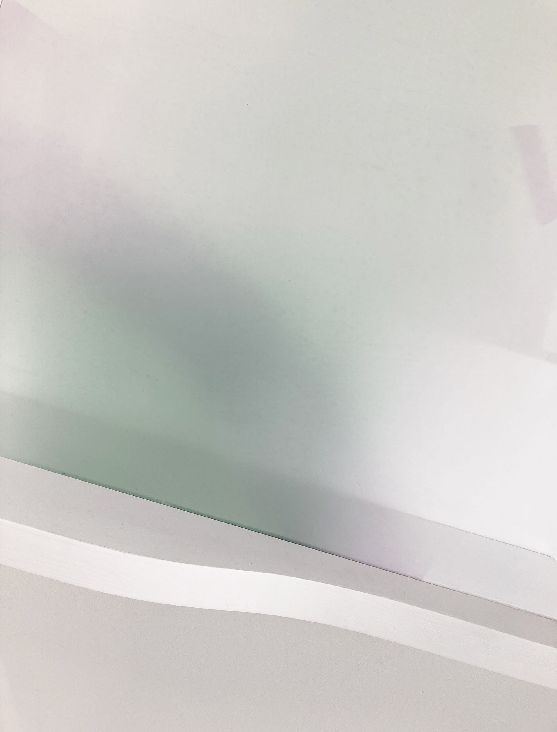 A close up of a curved white shelf supporting a printed acrylic sheet, with blurry green and purple forms.