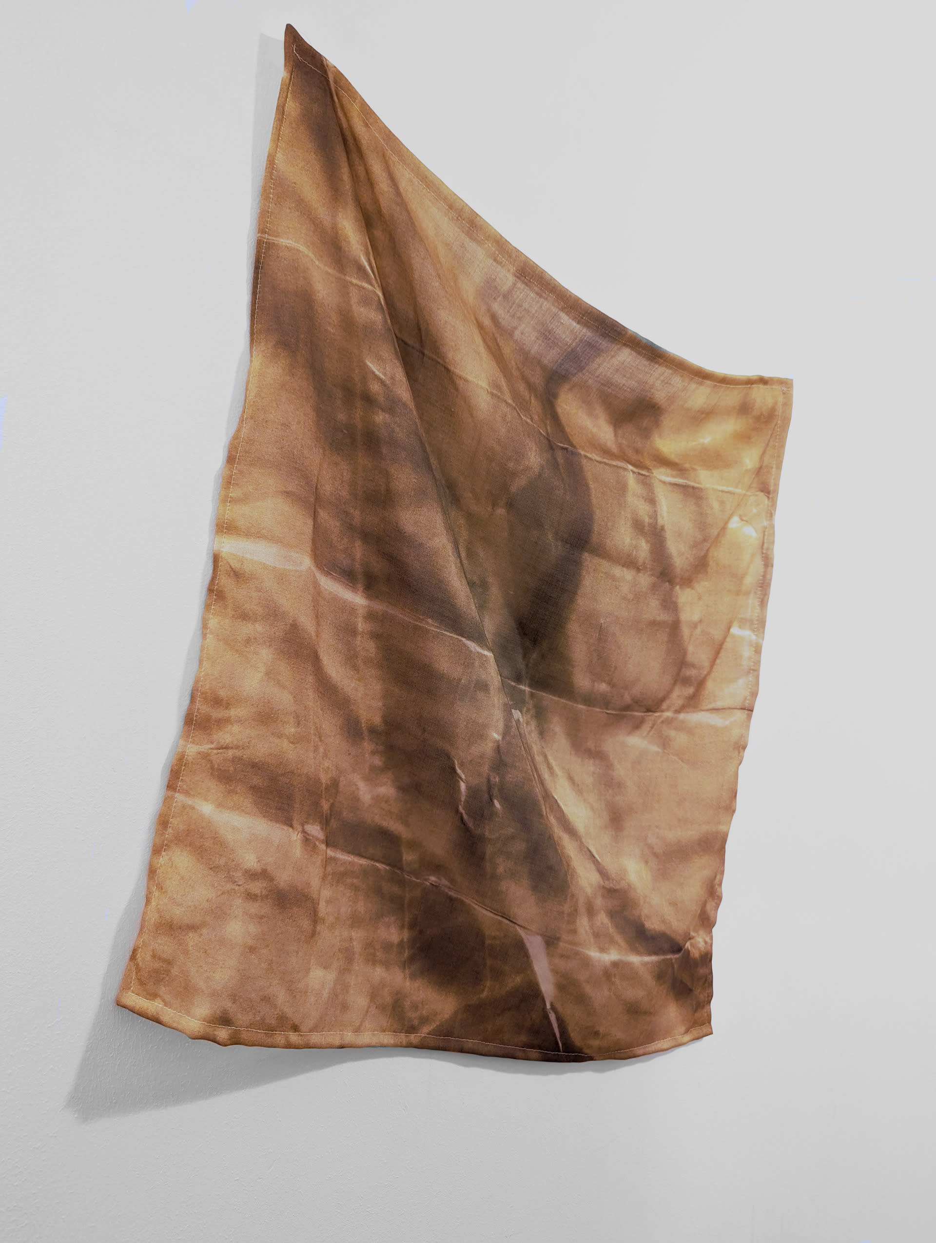 An orange and brown hued wool and silk textile hung on a white wall. illusions on bed folds and creases on the surface