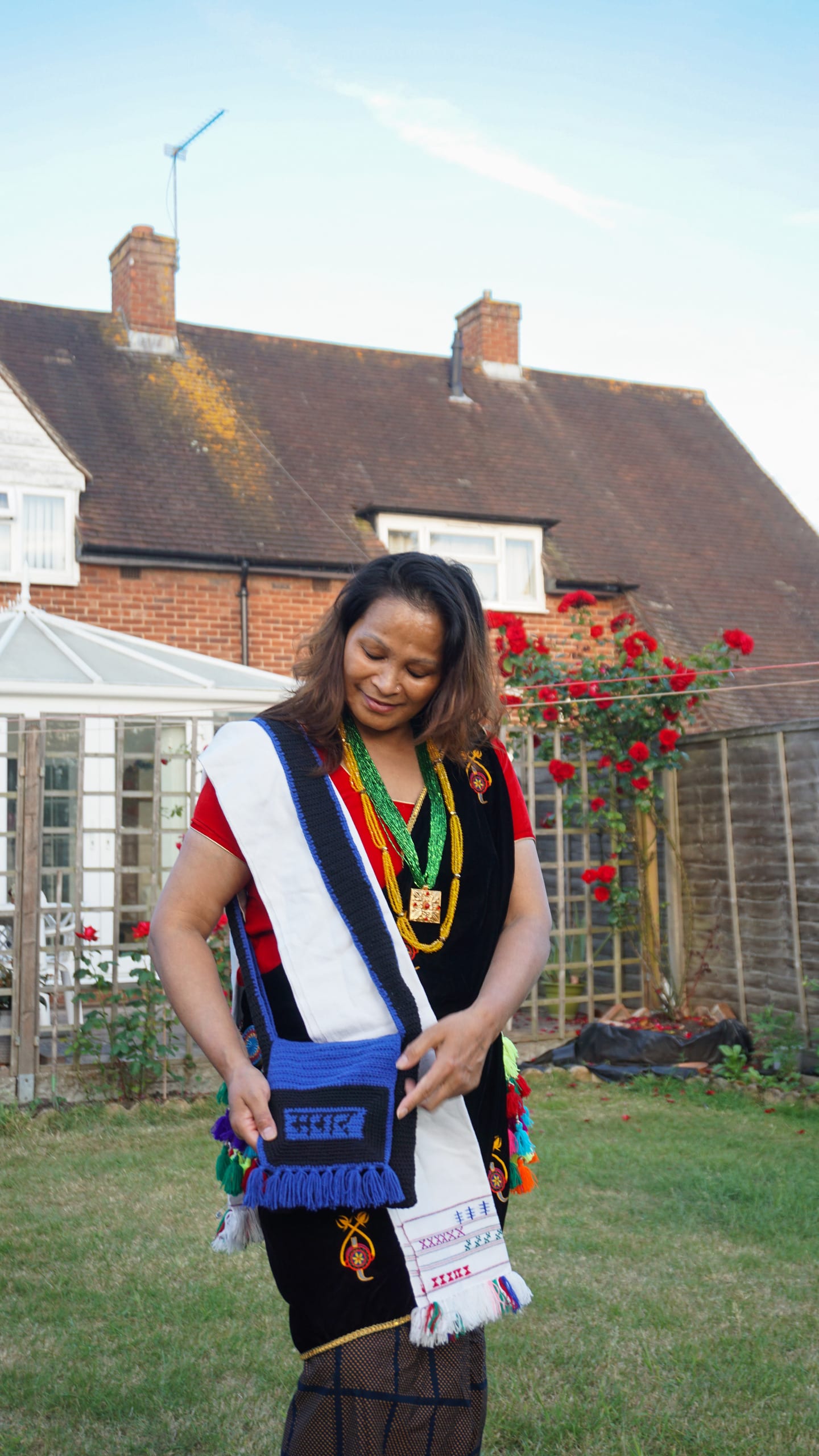 Ashmina's mother in traditional Magar clothing in her garden posing with crocheted bag Ashmina made