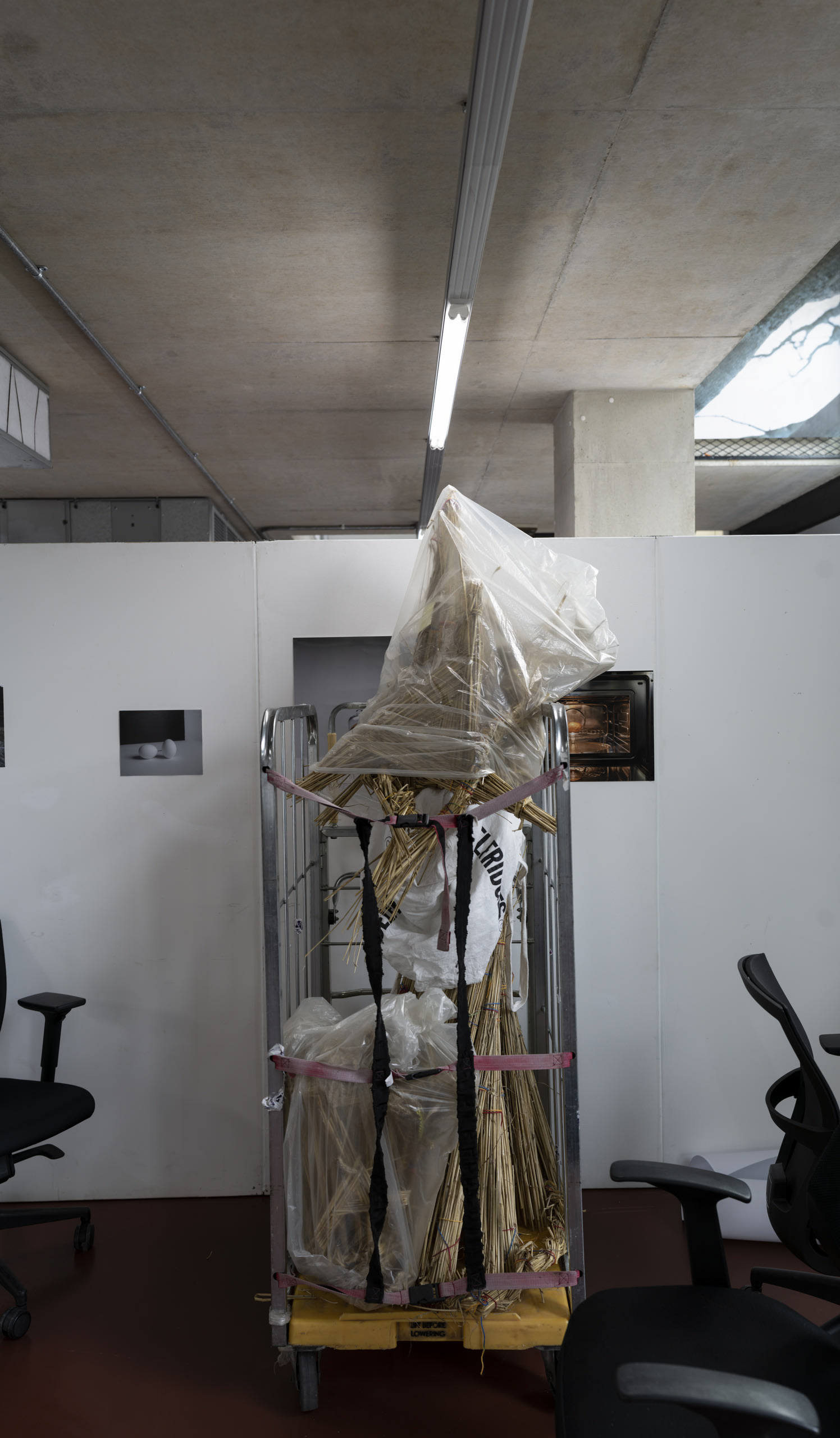 An image of a cart with a straw man inside, covered in bags and strapped in. The cart is surrounded by office chairs.