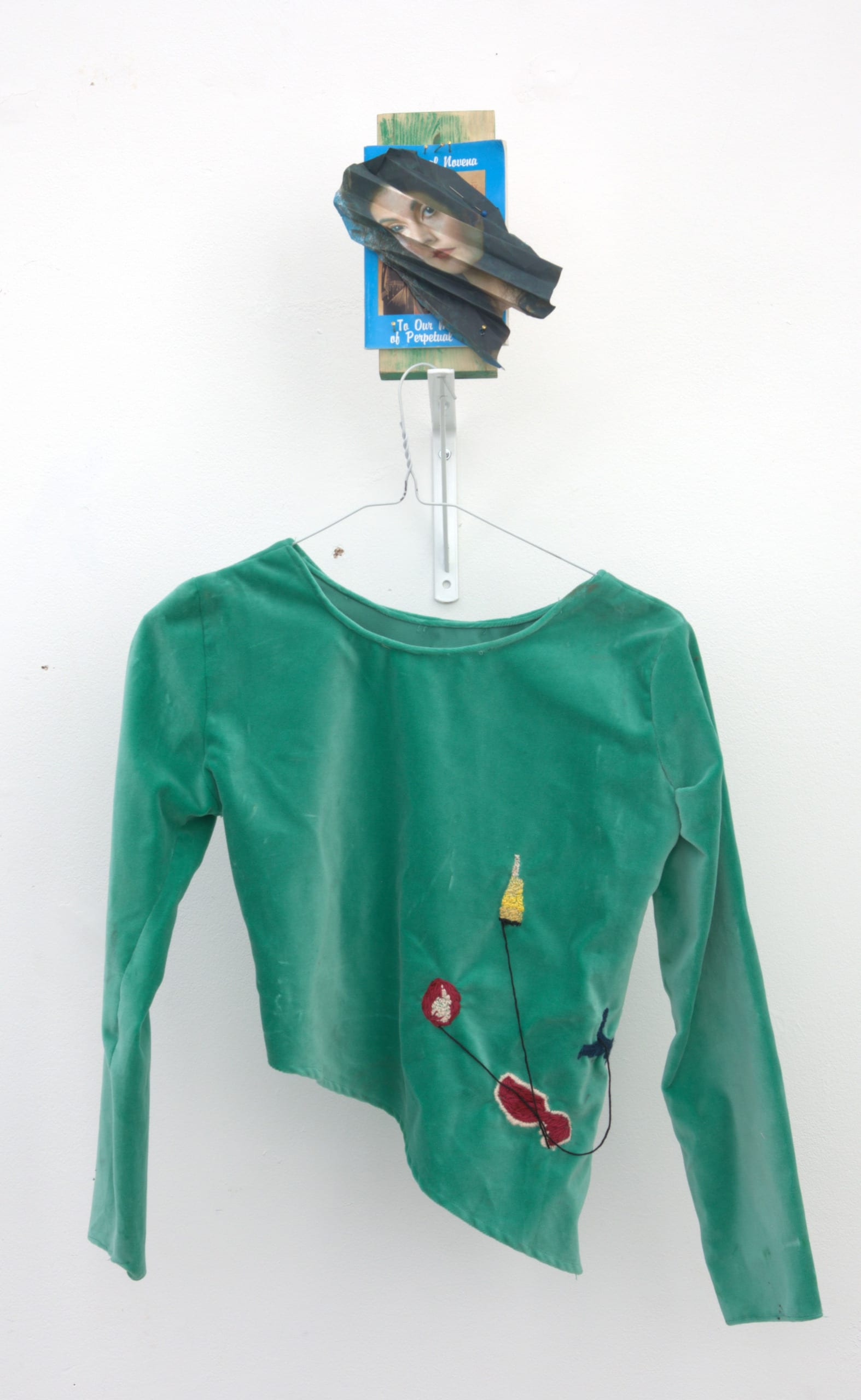 a handmade star trek costume hanging on a wall, below a wooden block with a paper collage with a portrait attached to the wood