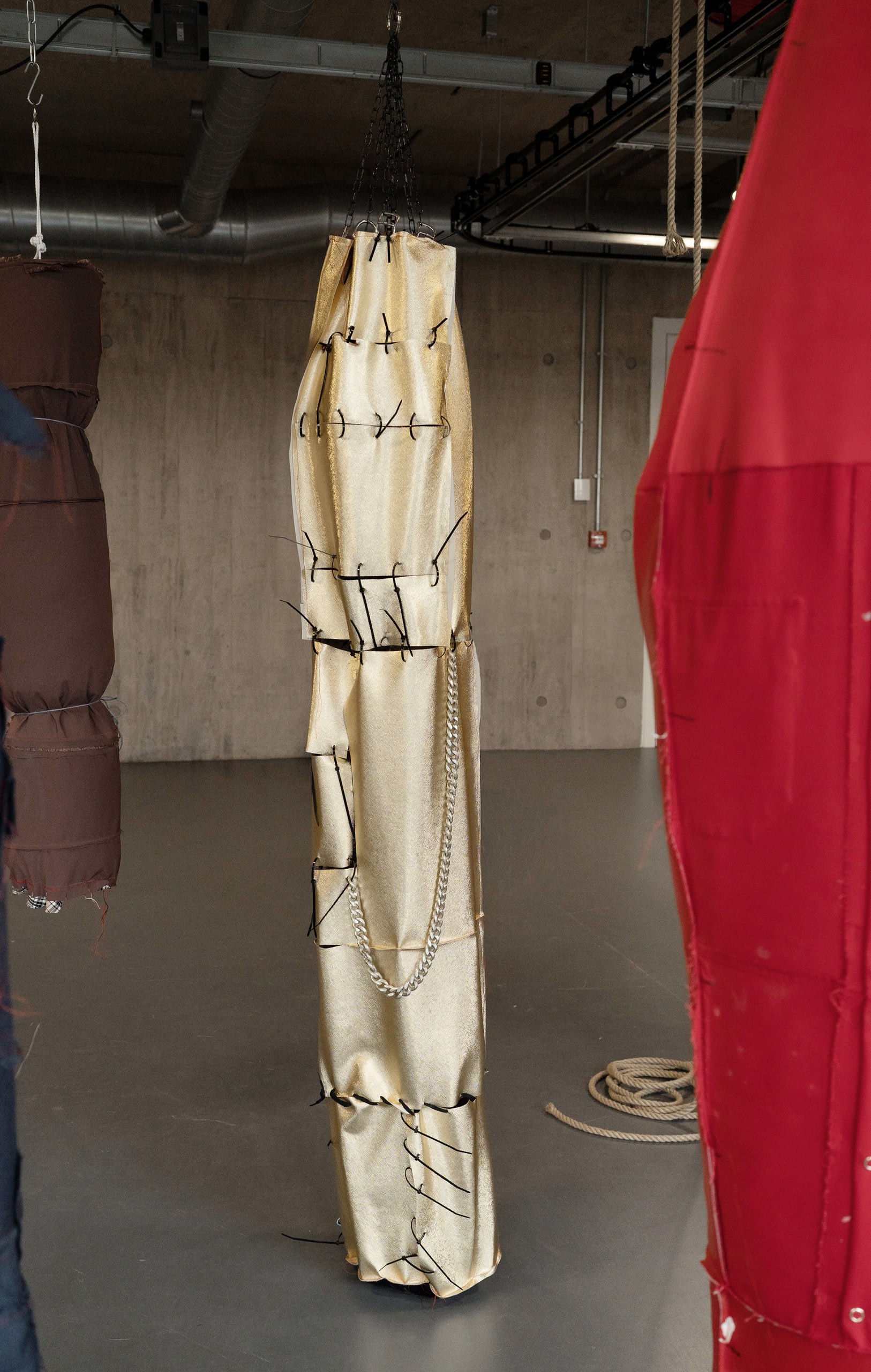 A bright gold object resembling a punch bag hanging by black chain. It is flaccid and empty, parts held together with cable ties