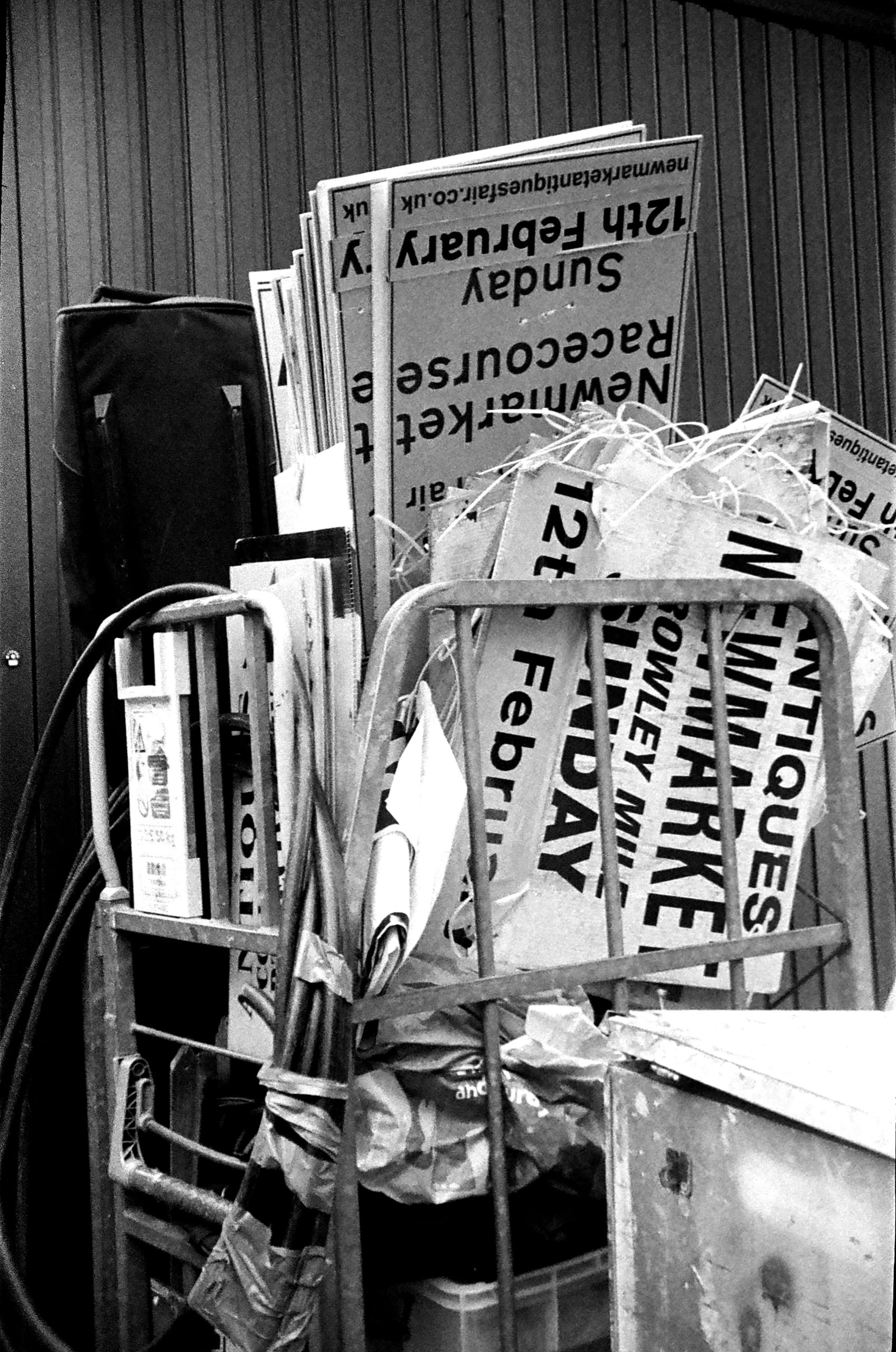 in a bin sits squashed and dilapidated signs for the market, there are lots of them rammed in upside-down, rubbish surrounds  