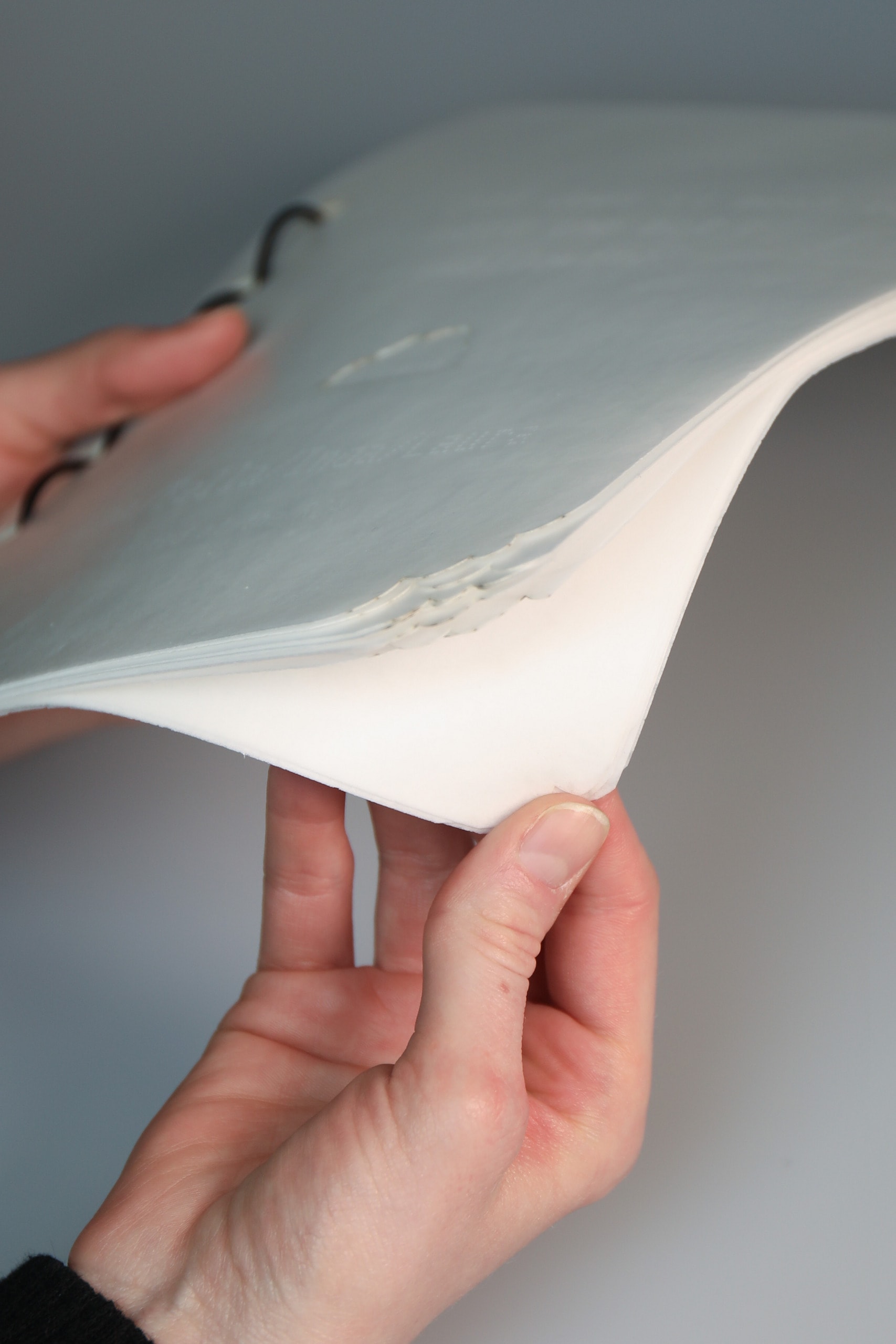 Photograph of two hands flicking through the edible booklet, the corners of which appear to have been nibbled
