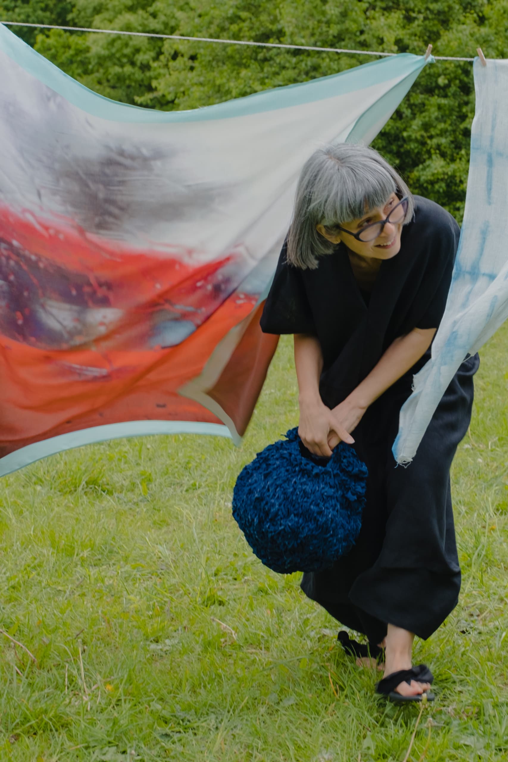 Jen ducks under a washing line holding silk and cotton scarves she has printed and hand dyed with natural indigo