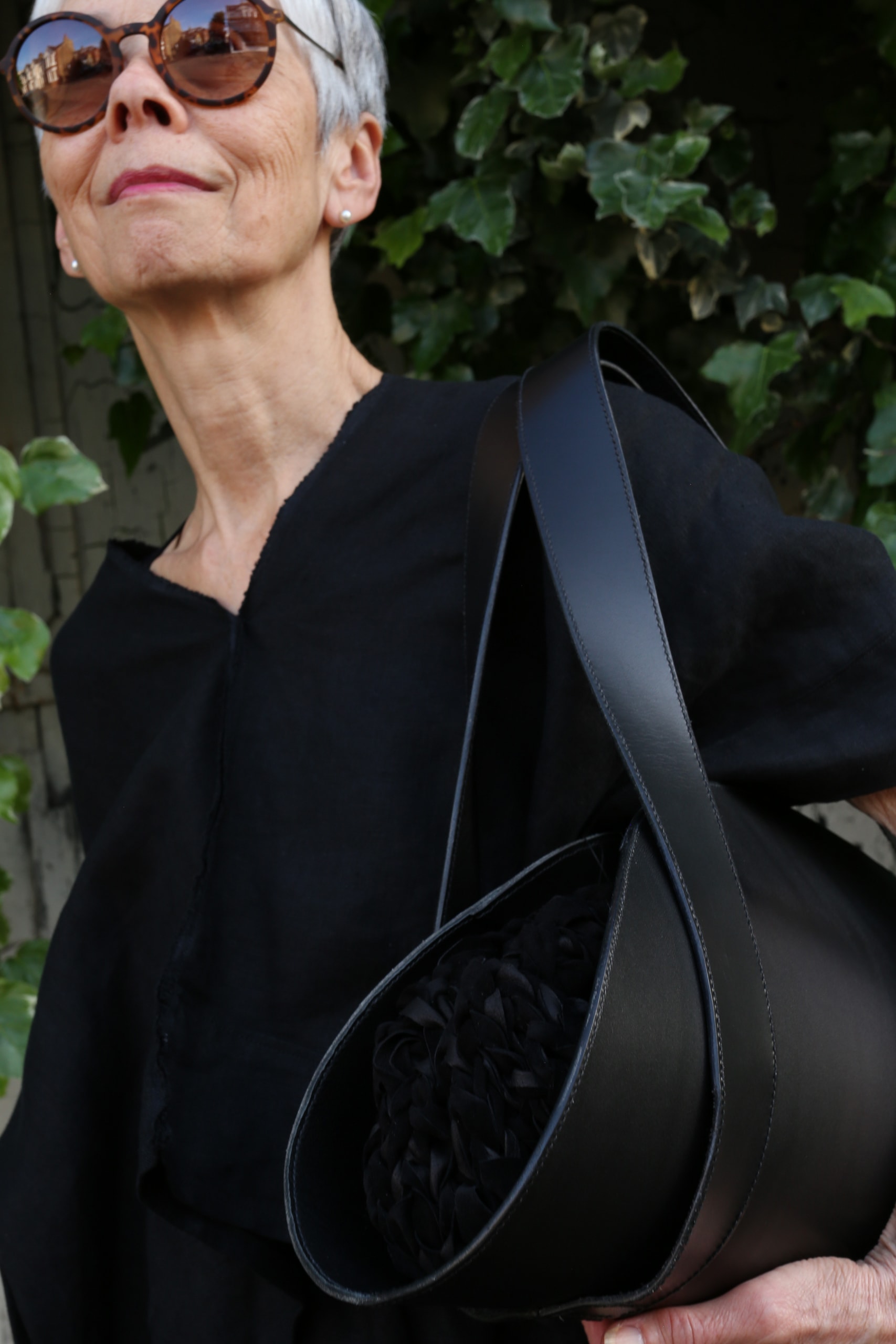 Wearing black linen and shades, the sophisticated older model holds the Pogi black leather and knitted suede bag