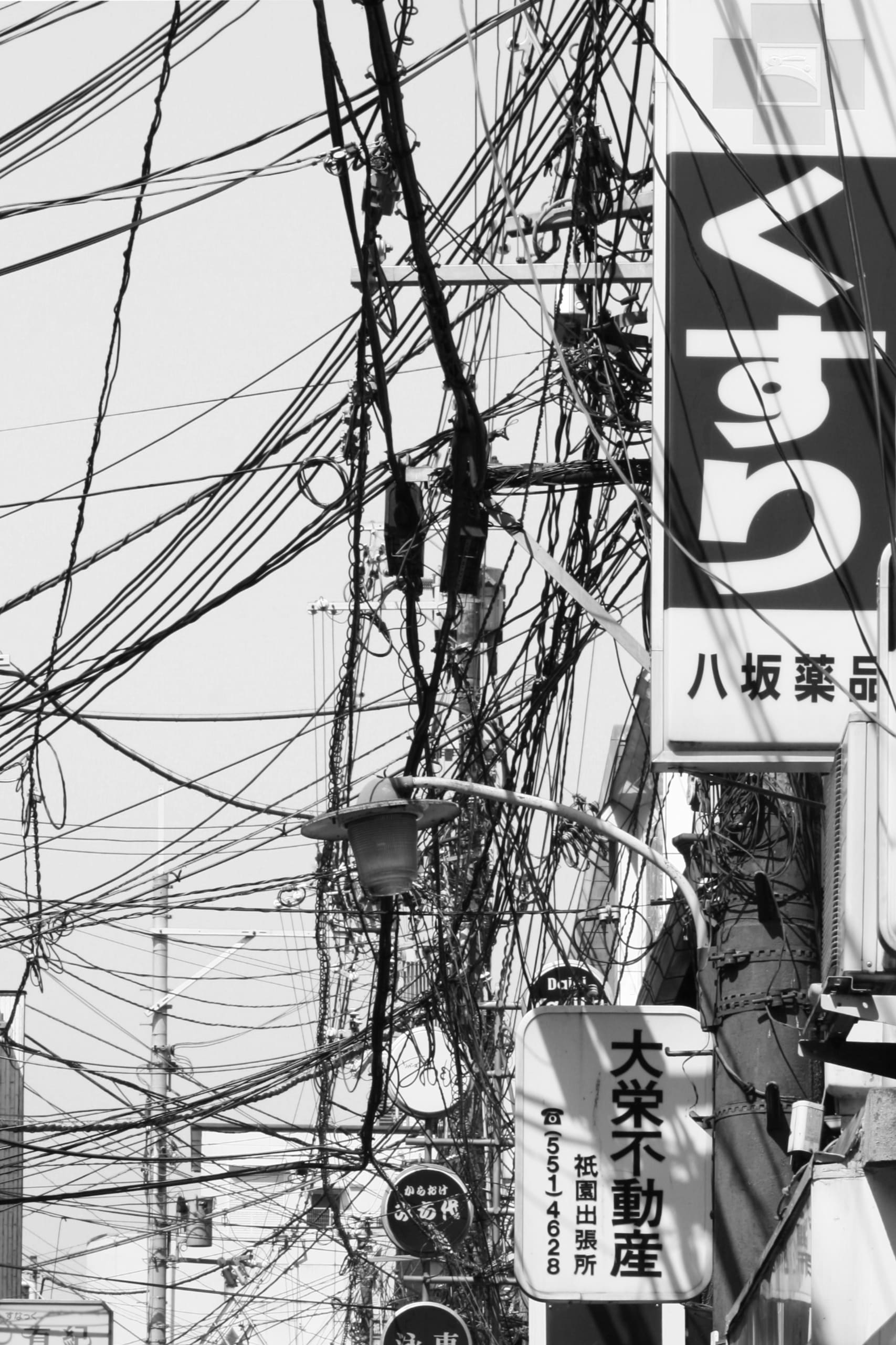 Black and white photo of excessive draping wires in Japan with a sign in Hirigana  kusuri meaning medicine in Japanese