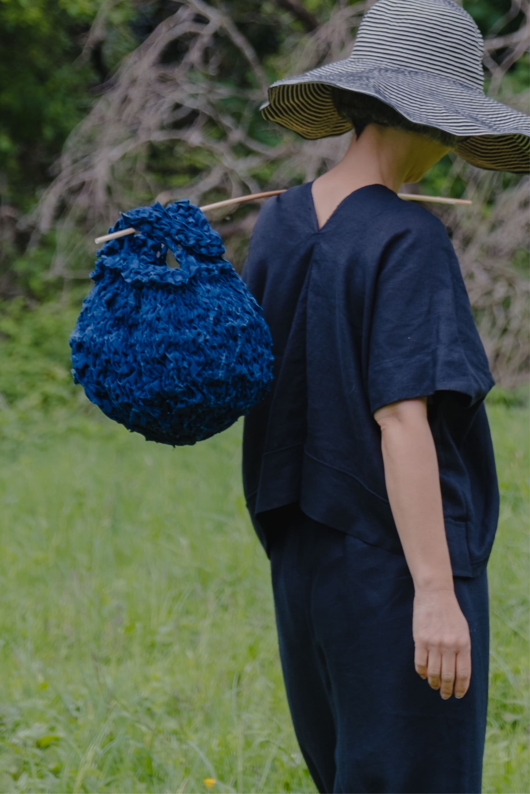 Jen faces away wearing the floppy hat with the blue mini sakk on a stick over her shoulder