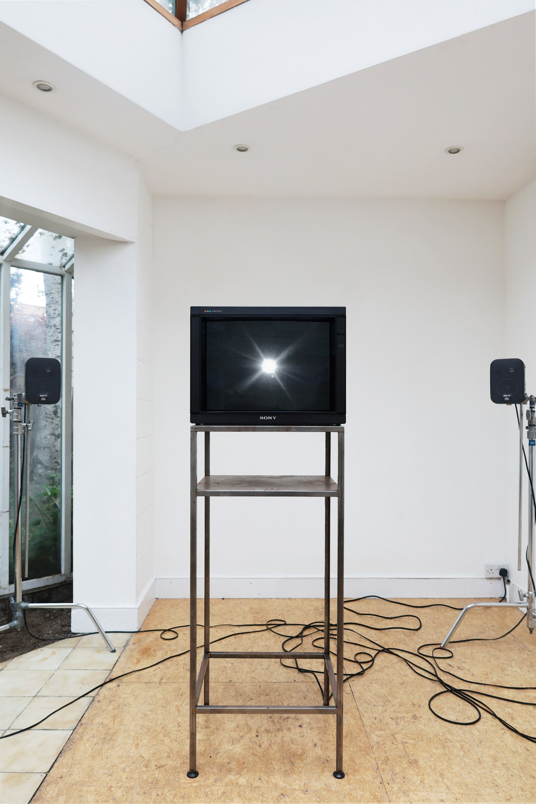 room with a large monitor on a metal stand with two speakers at the sides