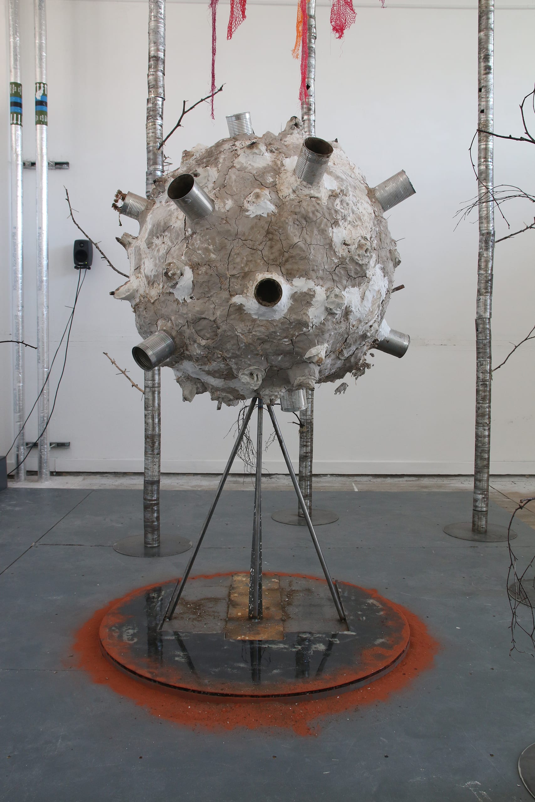 The central sculpture made of cracked clay, plaster, burnt twigs & tin cans resembles an atom, moon or a meteorite from space. 