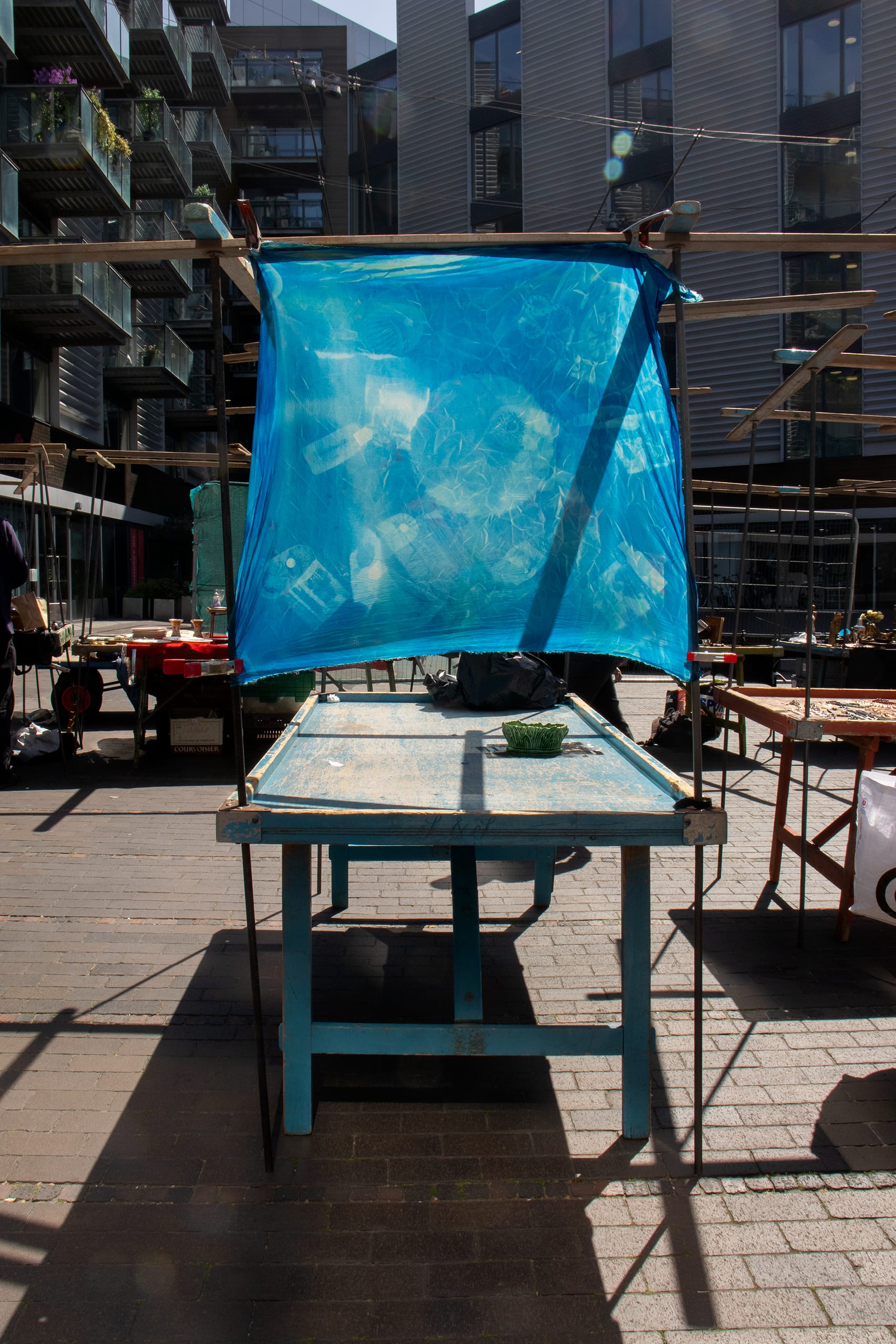 A blue piece of material is stretched over a market stall, it has images exposed onto it 