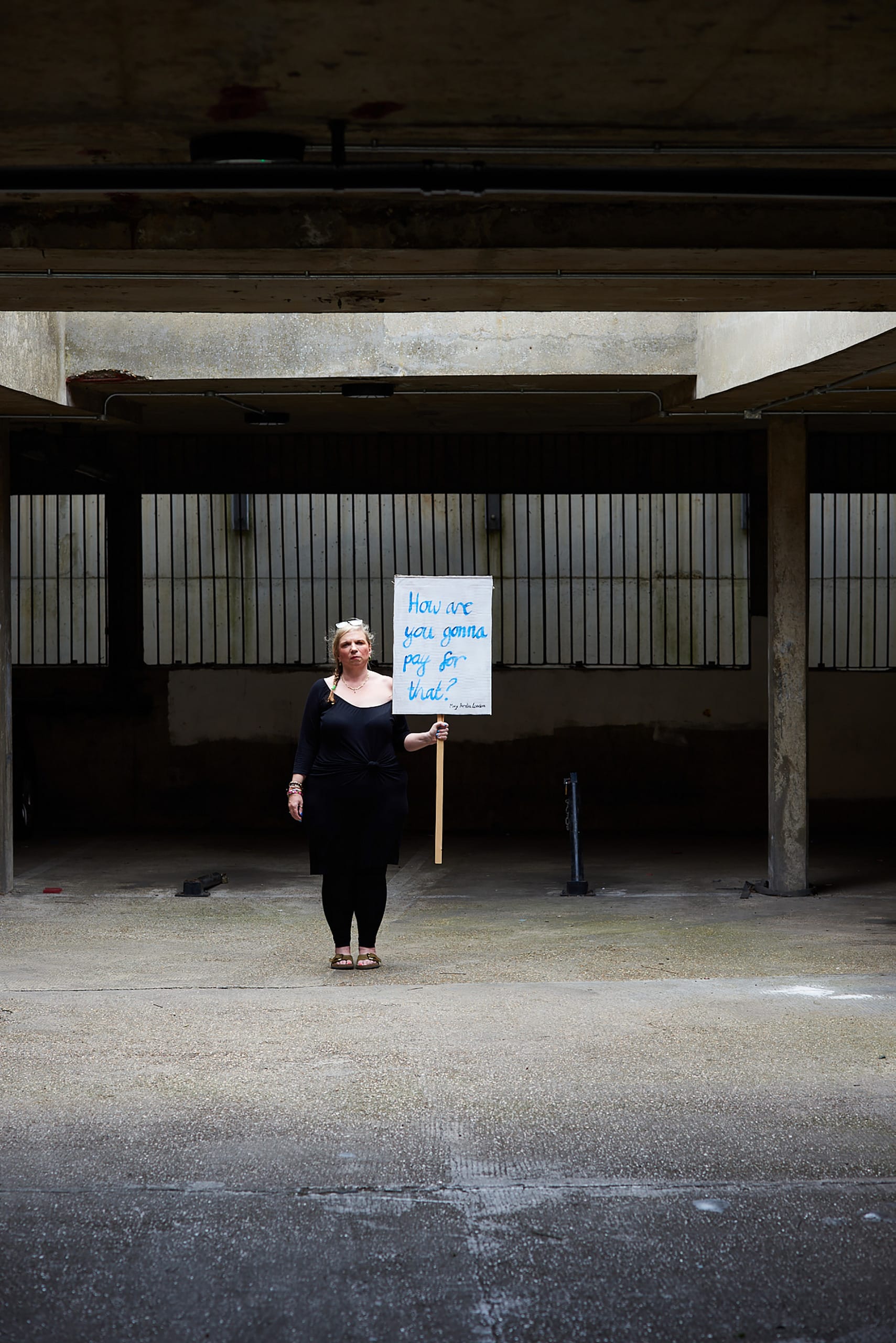 Mary Amelia London stands holding a sign saying: 'How are you gonna pay for that?'