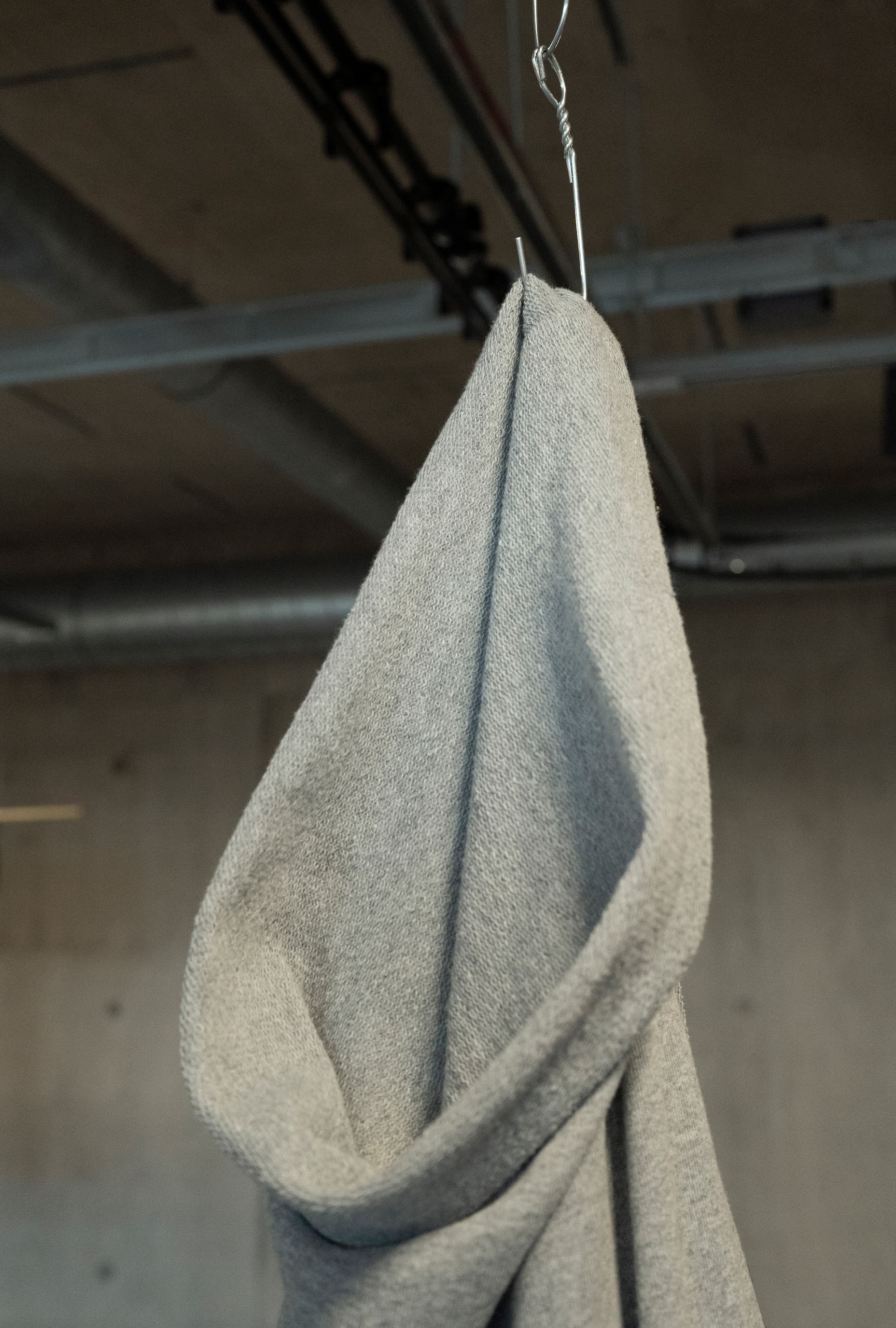 Close-up of grey stretch material forming the opening of bag and resembling a hood, hanging from ceiling by bent metal hanger