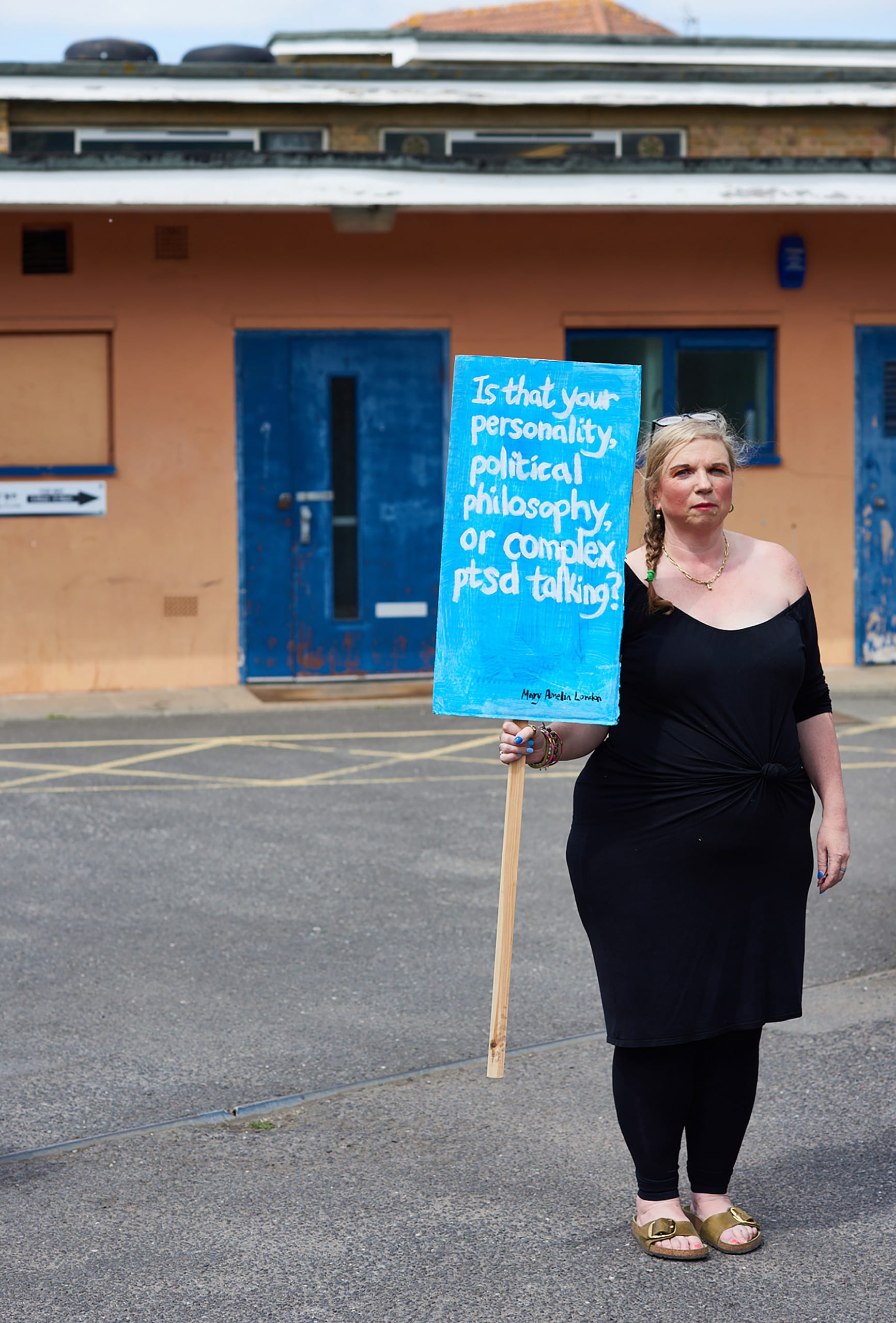 Mary Amelia London stands holding a sign saying: 'Is that your personality, your political philosophy or complex ptsd talking?'