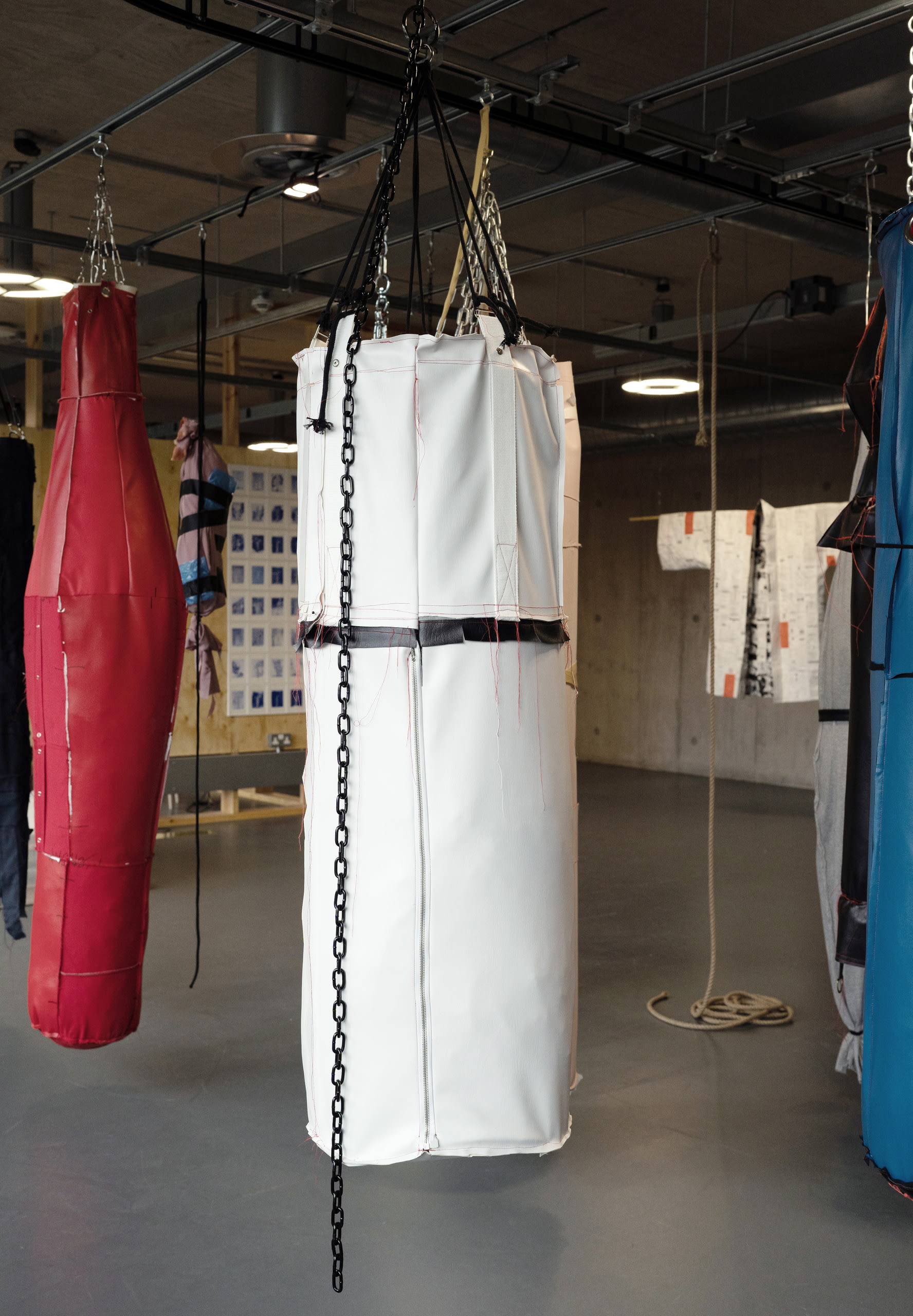 A big white leather object resembling a punch bag hanging by black chain. Parts of others hanging in the periphery