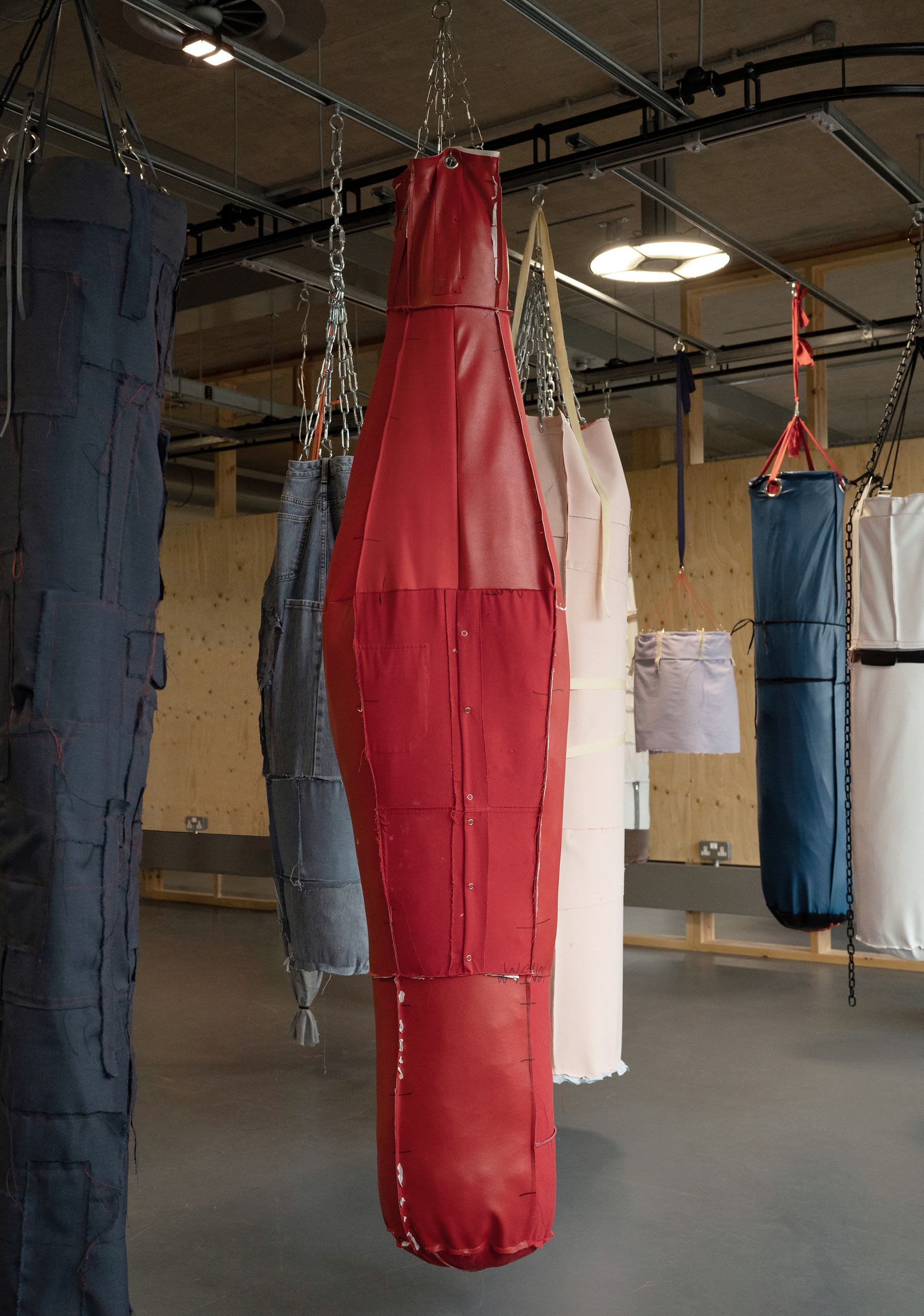 One large red object resembling a punch bag hanging by thick chain, with parts of others hanging nearby