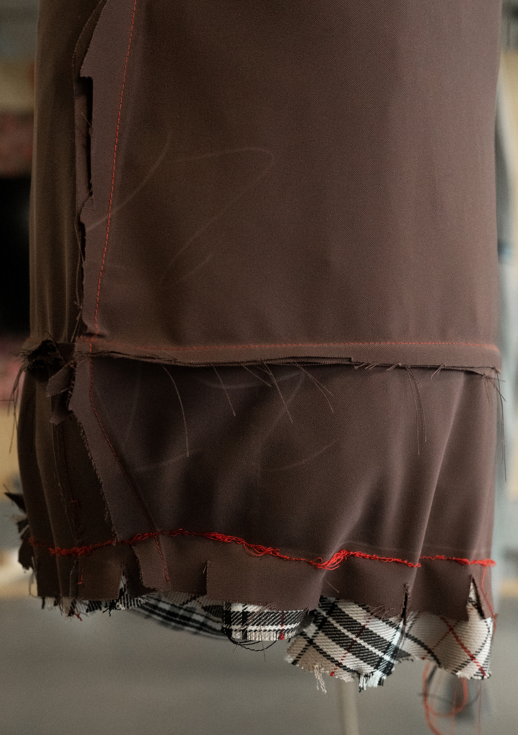 Close-up detail of brown fabric with faint chalk markings from its construction, with ragged seams and red thread exposed