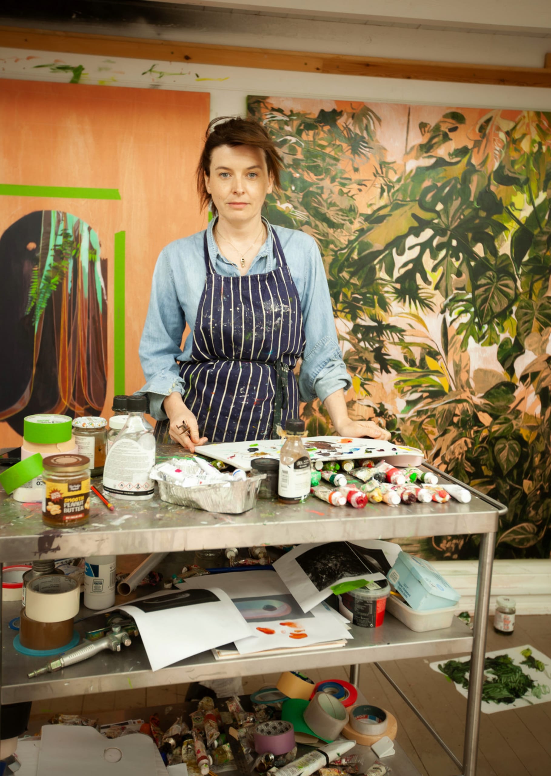 portrait of Nina Ogden in her painting studio with a paint palette on a trolley in front of her.