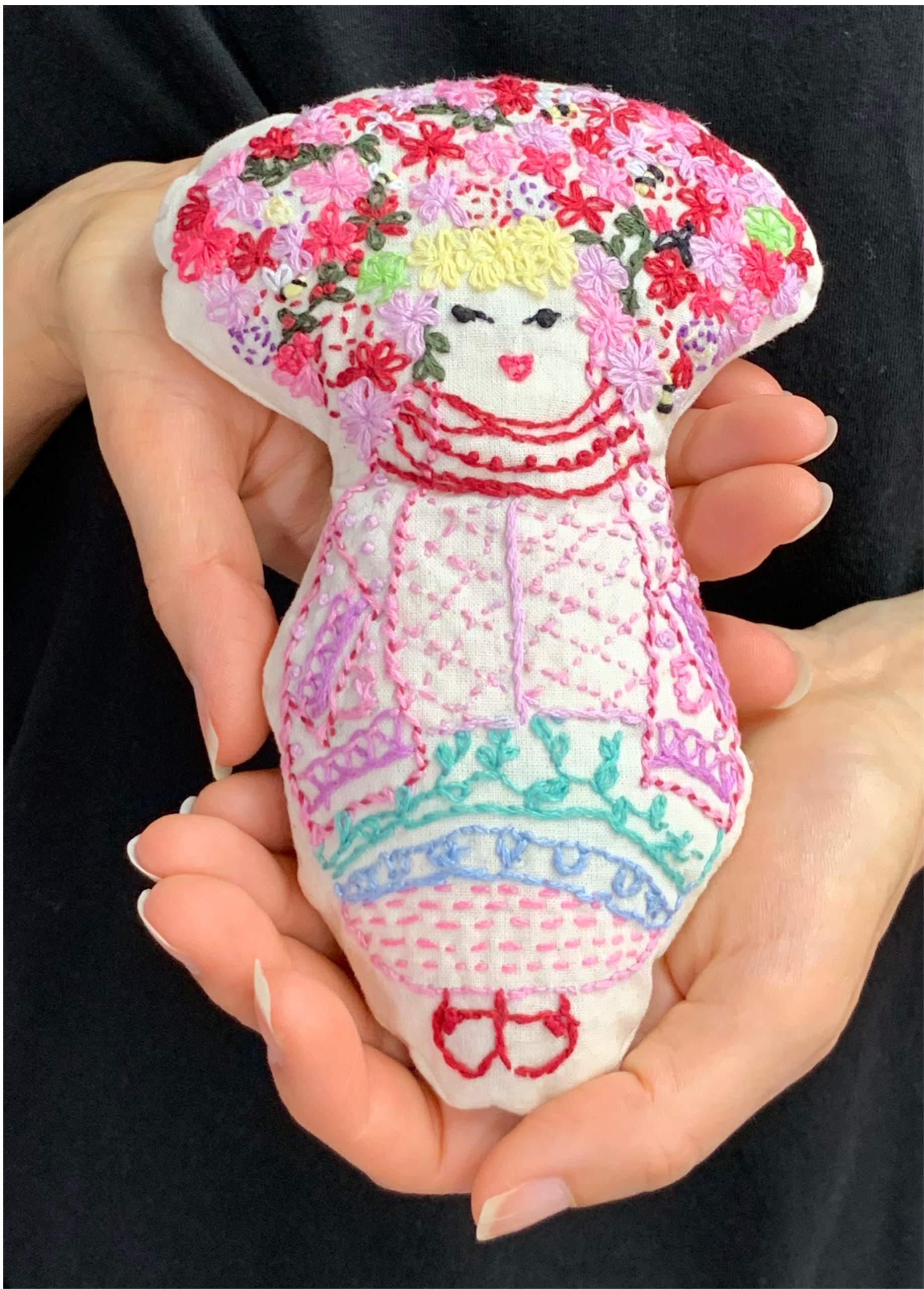 Jen holds a small, hand embroidered doll, that wears a massive flowered headdress