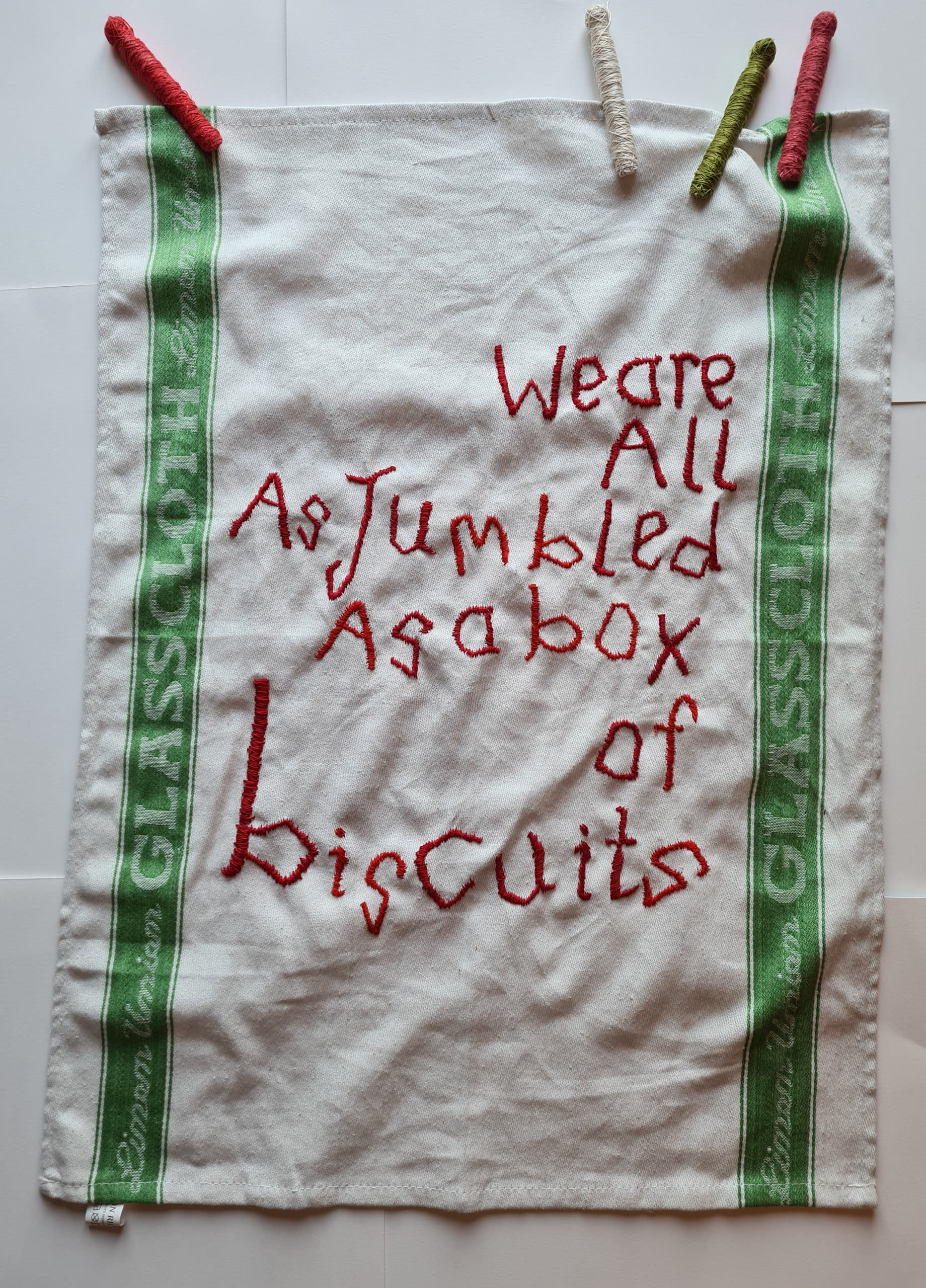 glass cloth embroidered with We are All as Jumbled as a box of biscuits 