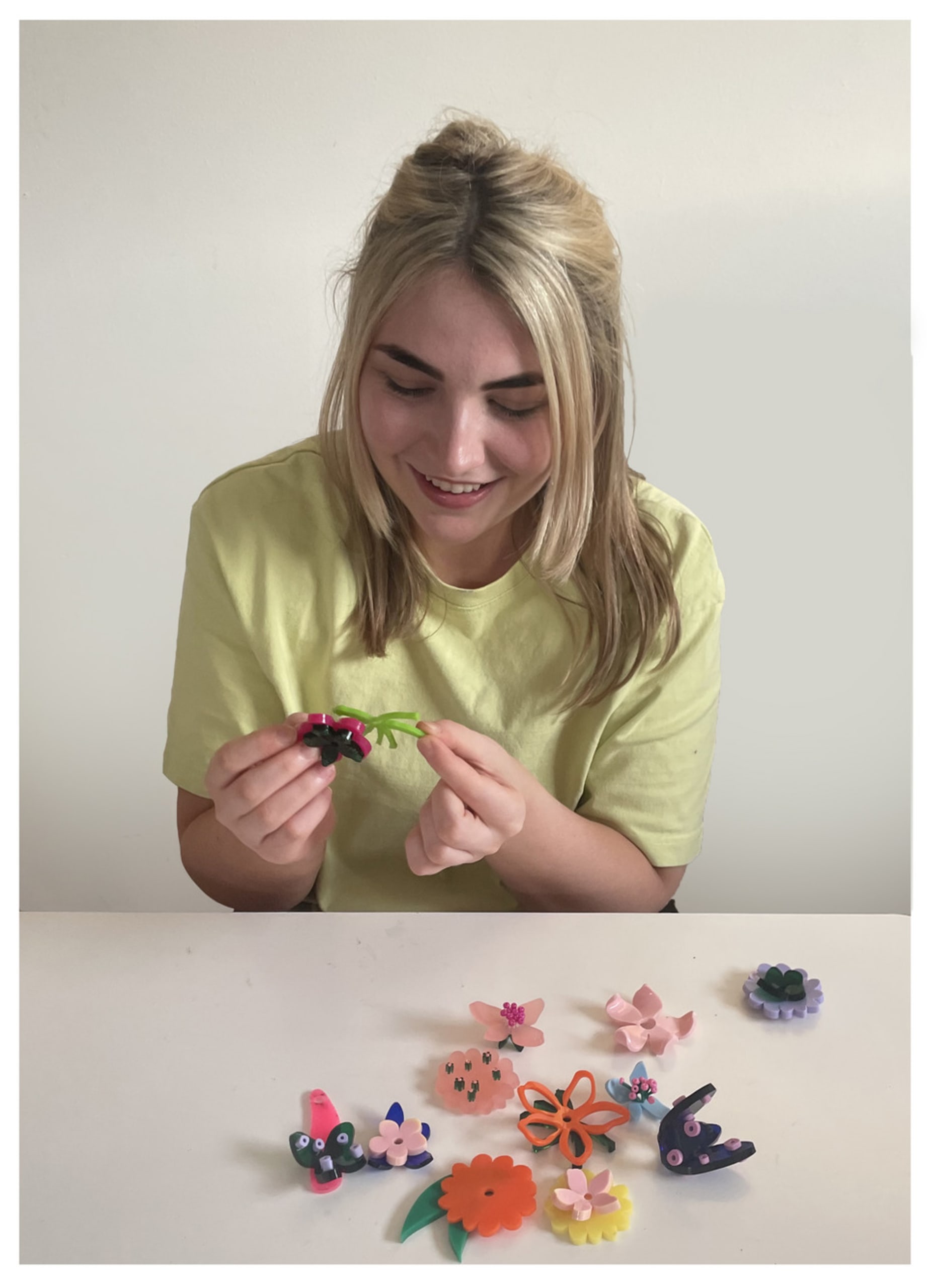 Hannah sat in front of a white wall with her models infront of her smiling looking at them.