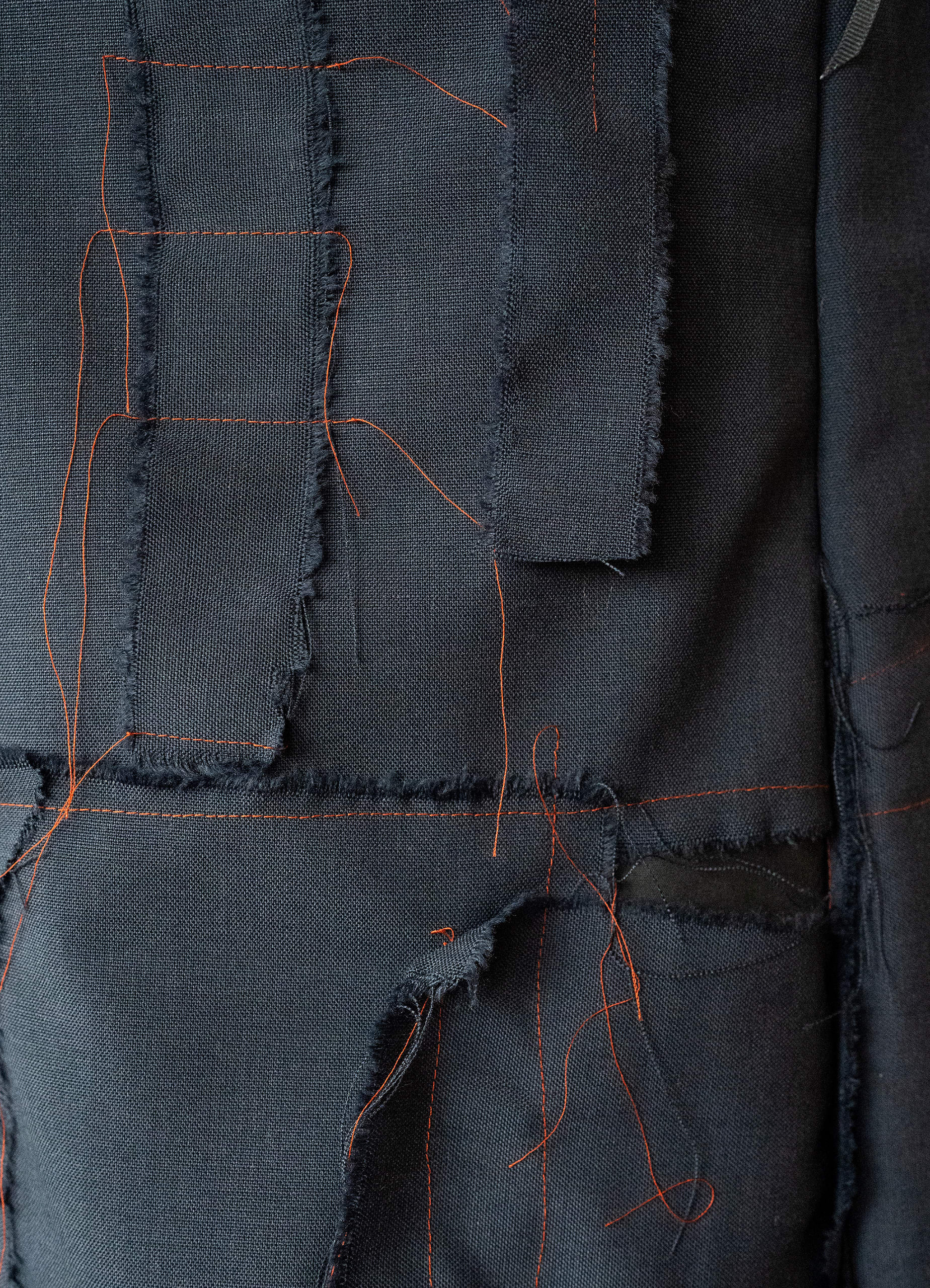 Close-up detail of ragged scraps of navy suit material held together with excessive red thread