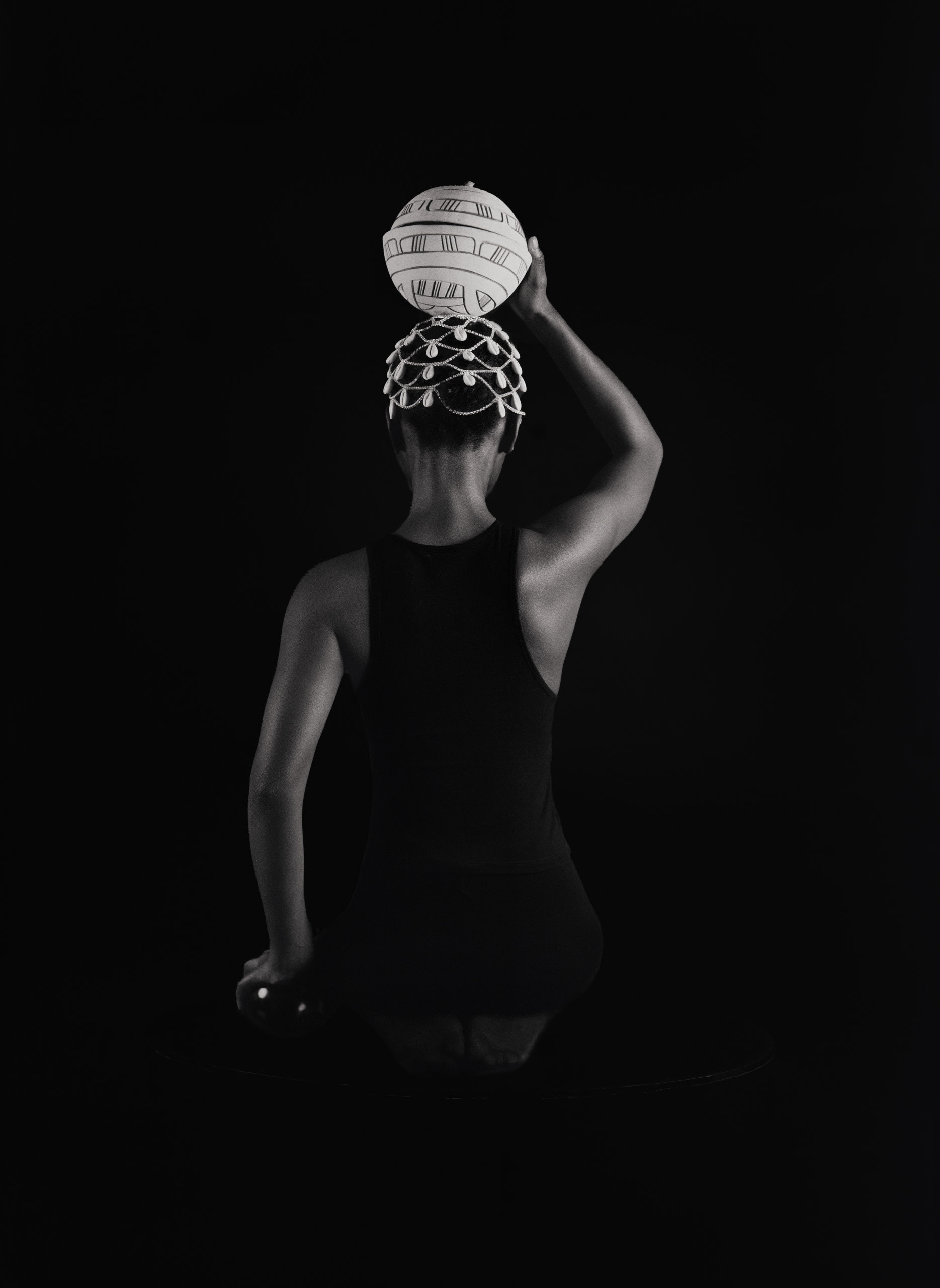 B and W image of a girl holding a calabash on her head