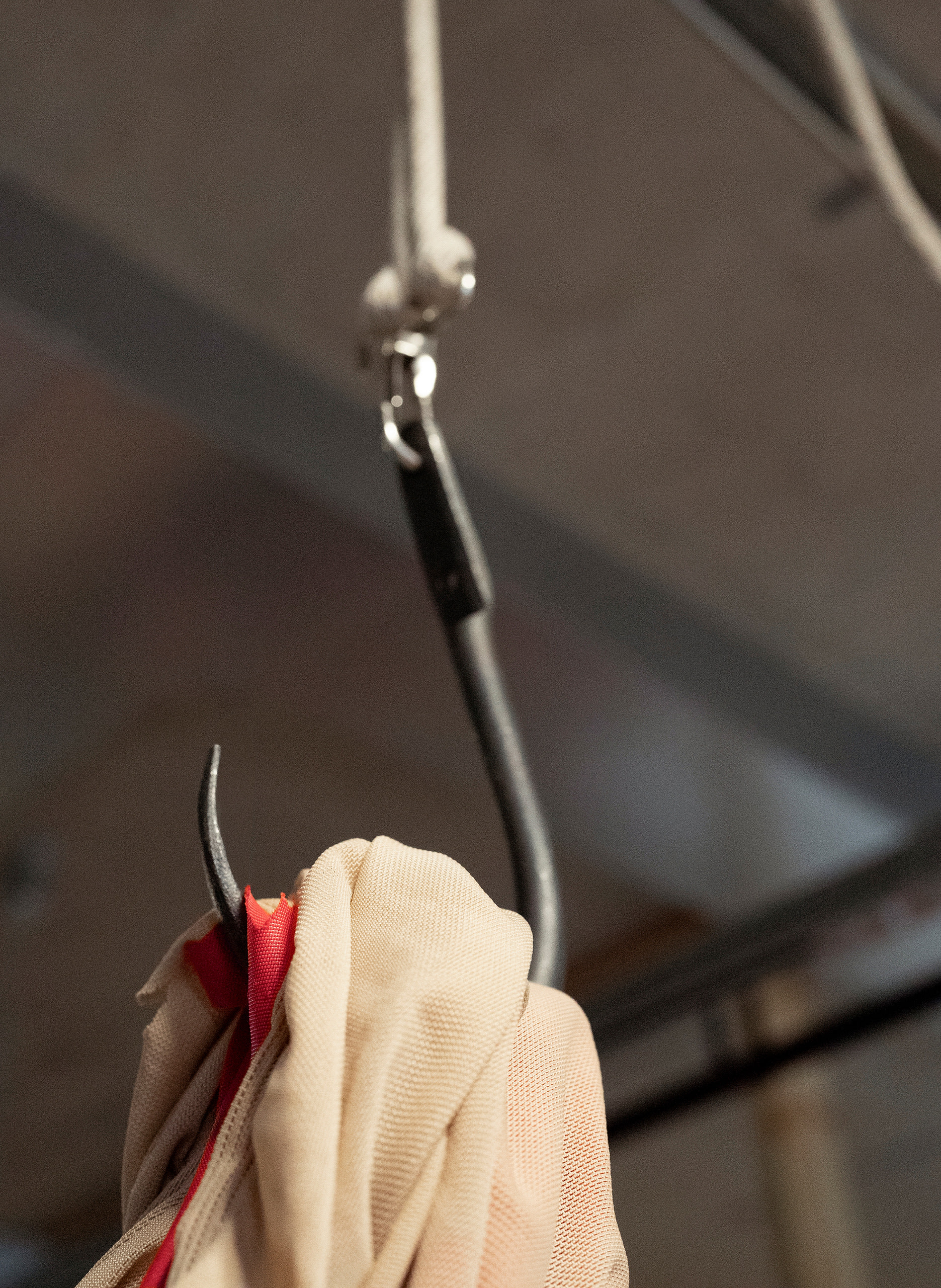 Close-up detail of wrought iron meathook with red and translucent beige material pierced and hanging from it