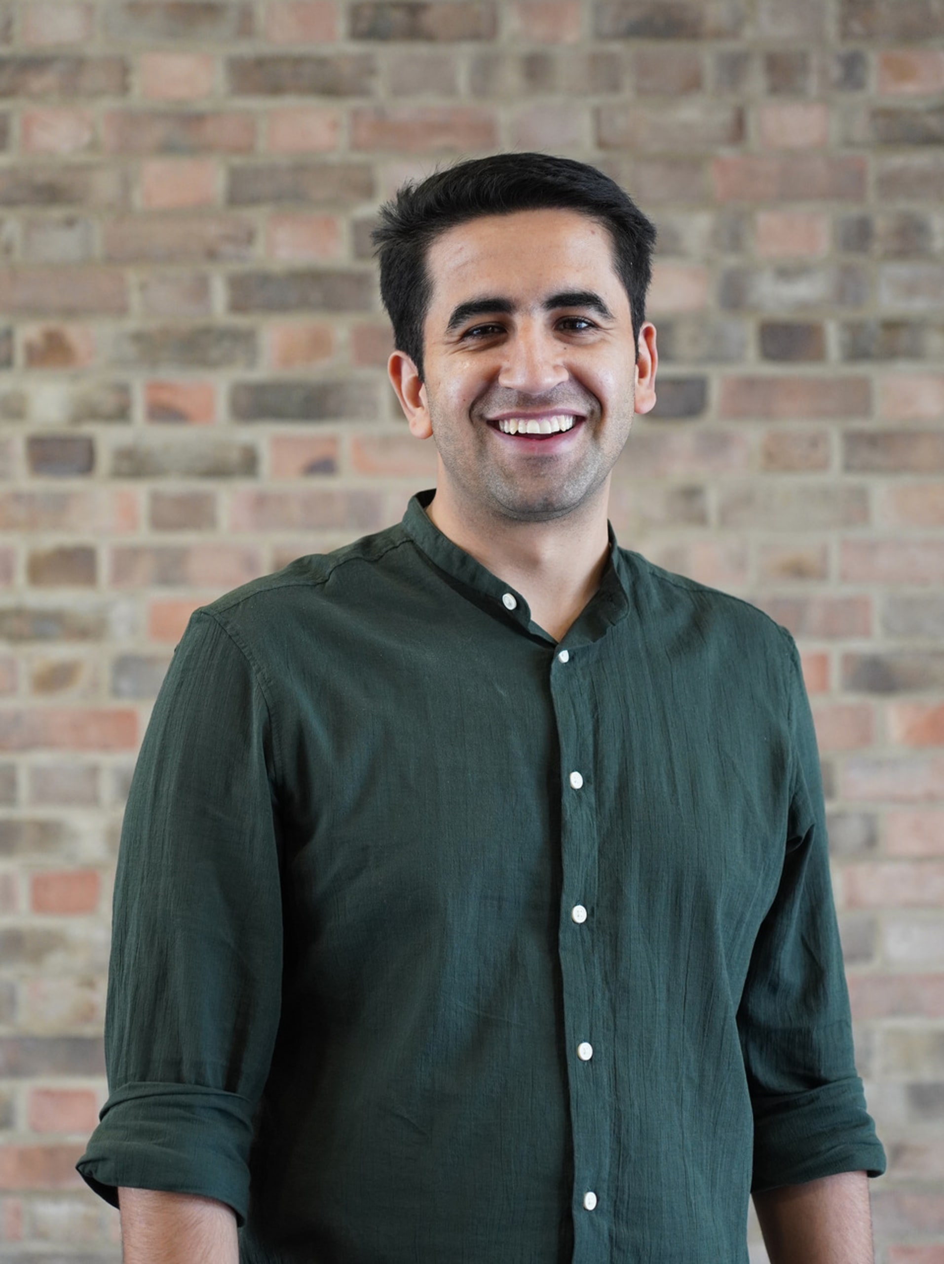 Design Engineer Sachin Mehra smiling in a green linen shirt on a bricked wall background