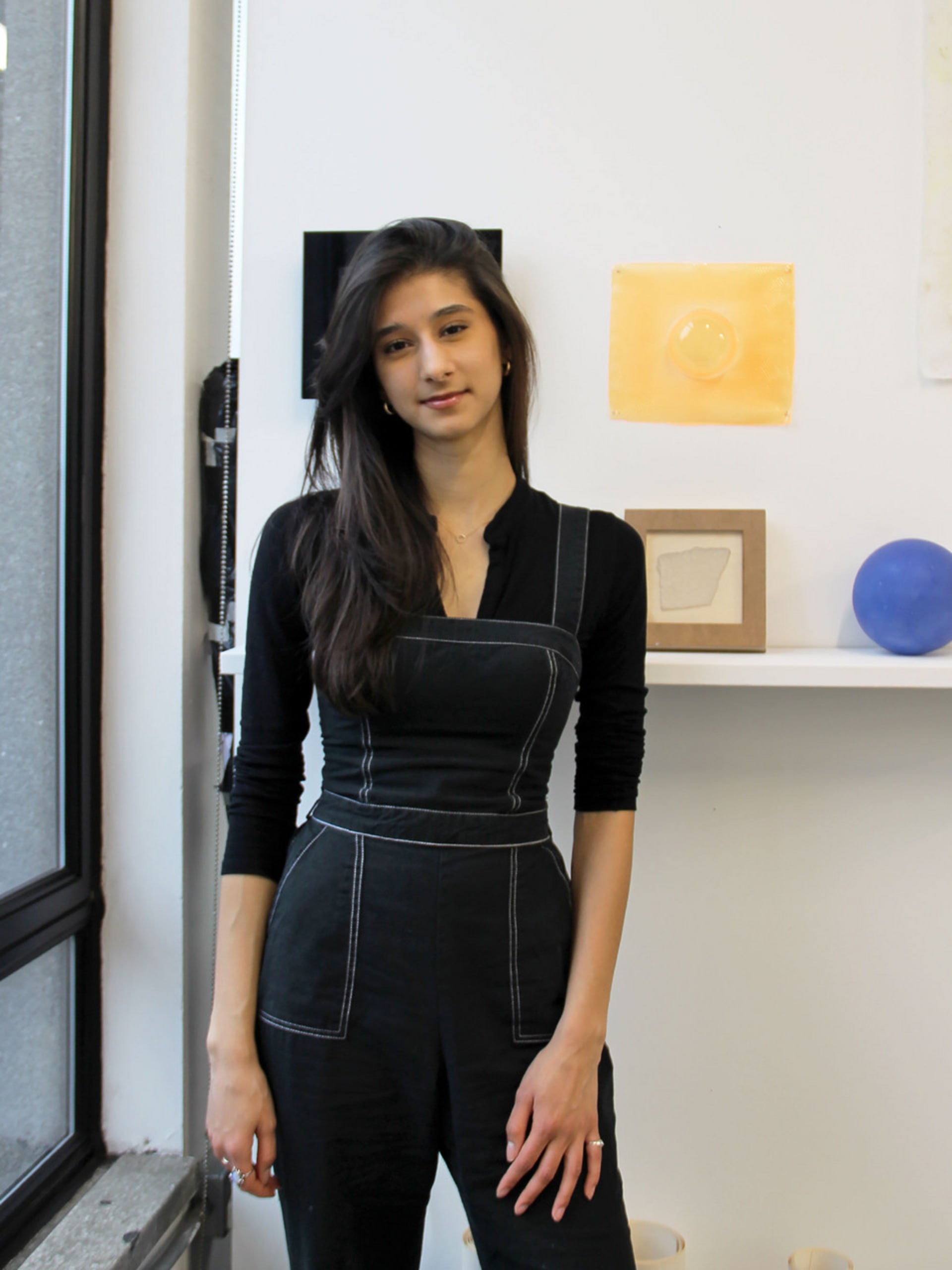 Girl standing in front of a white wall with orange and blue artworks hung.