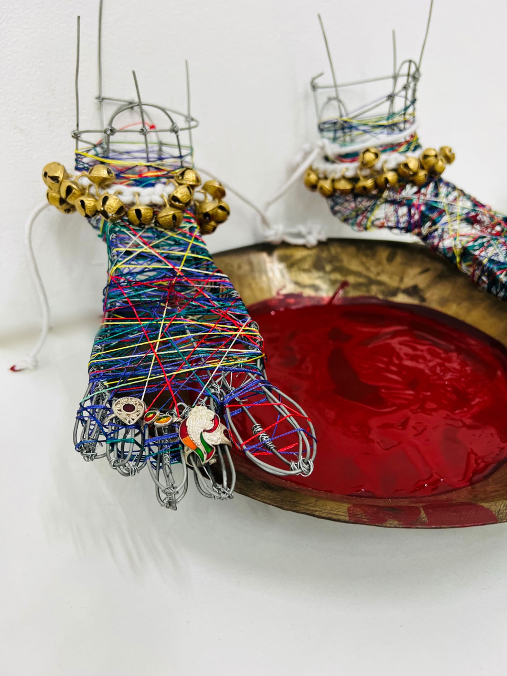 brass plate with maroonish paint and two feet made with wire, covered with colourful thread tied to each other with large bells.