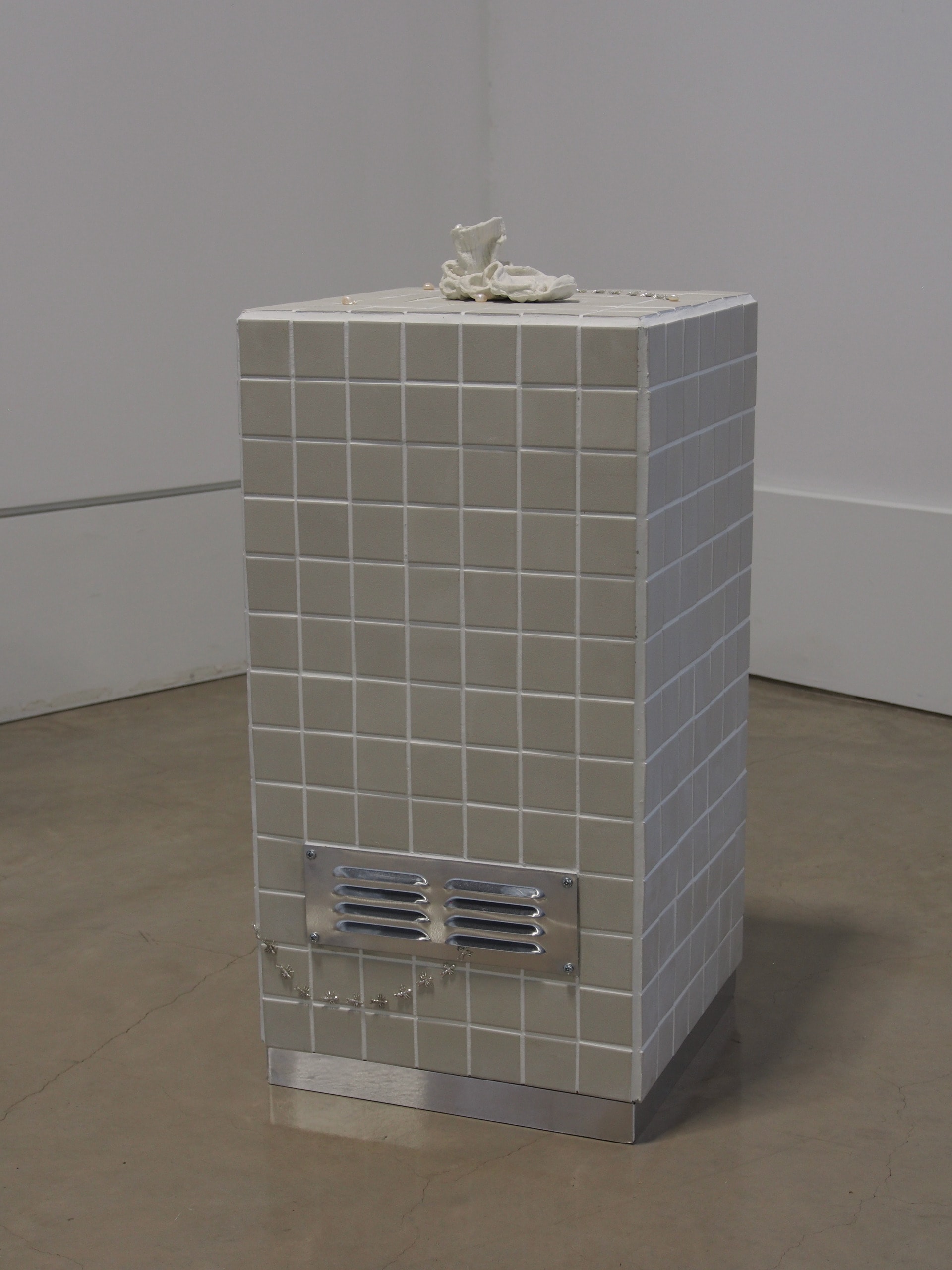 A cream tiled plinth with a metal vent on the side. Out of the vent crawls a trail of silver ants leading to a ceramic sock.