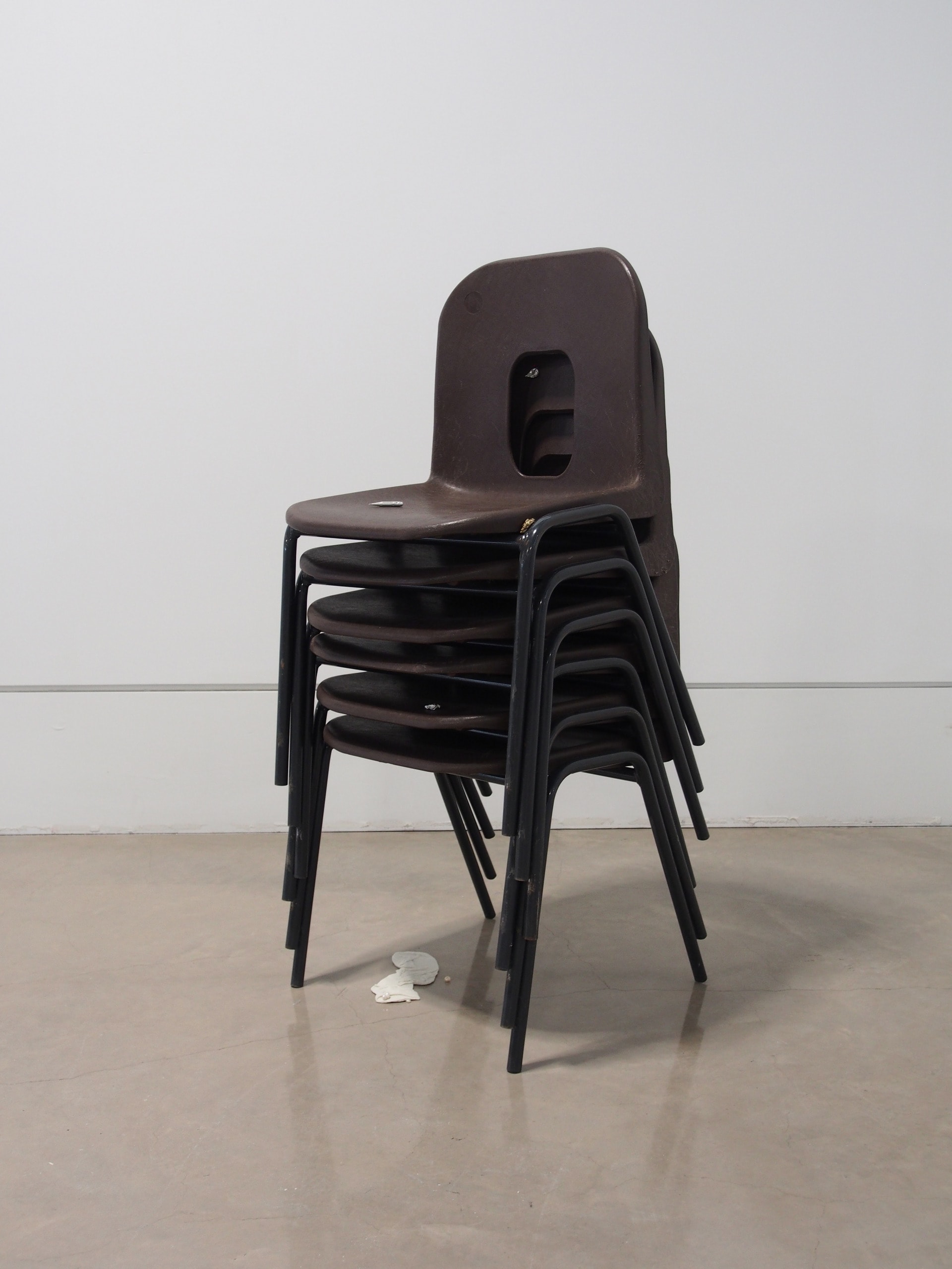 a stack of plastic chairs with a number of small silver and bronze sculptures on it, underneath is a ceramic sock