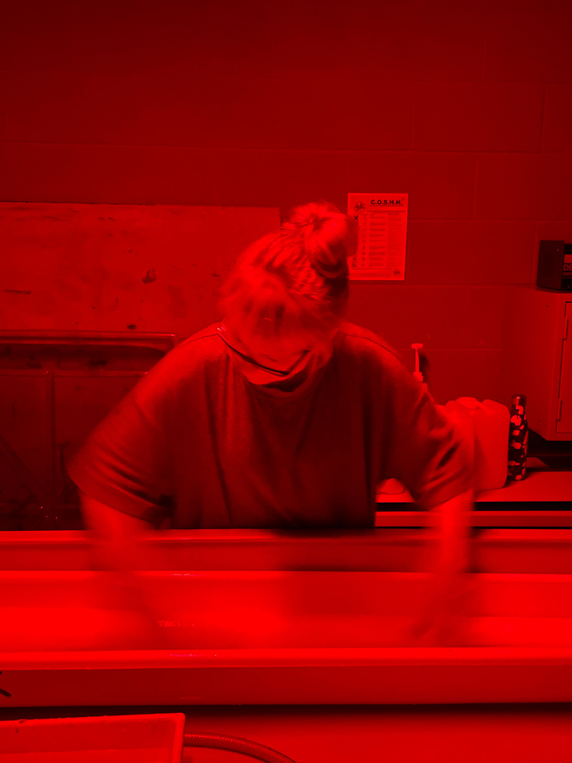 red photograph of a girl in the darkroom with her hands in a tray developing a print