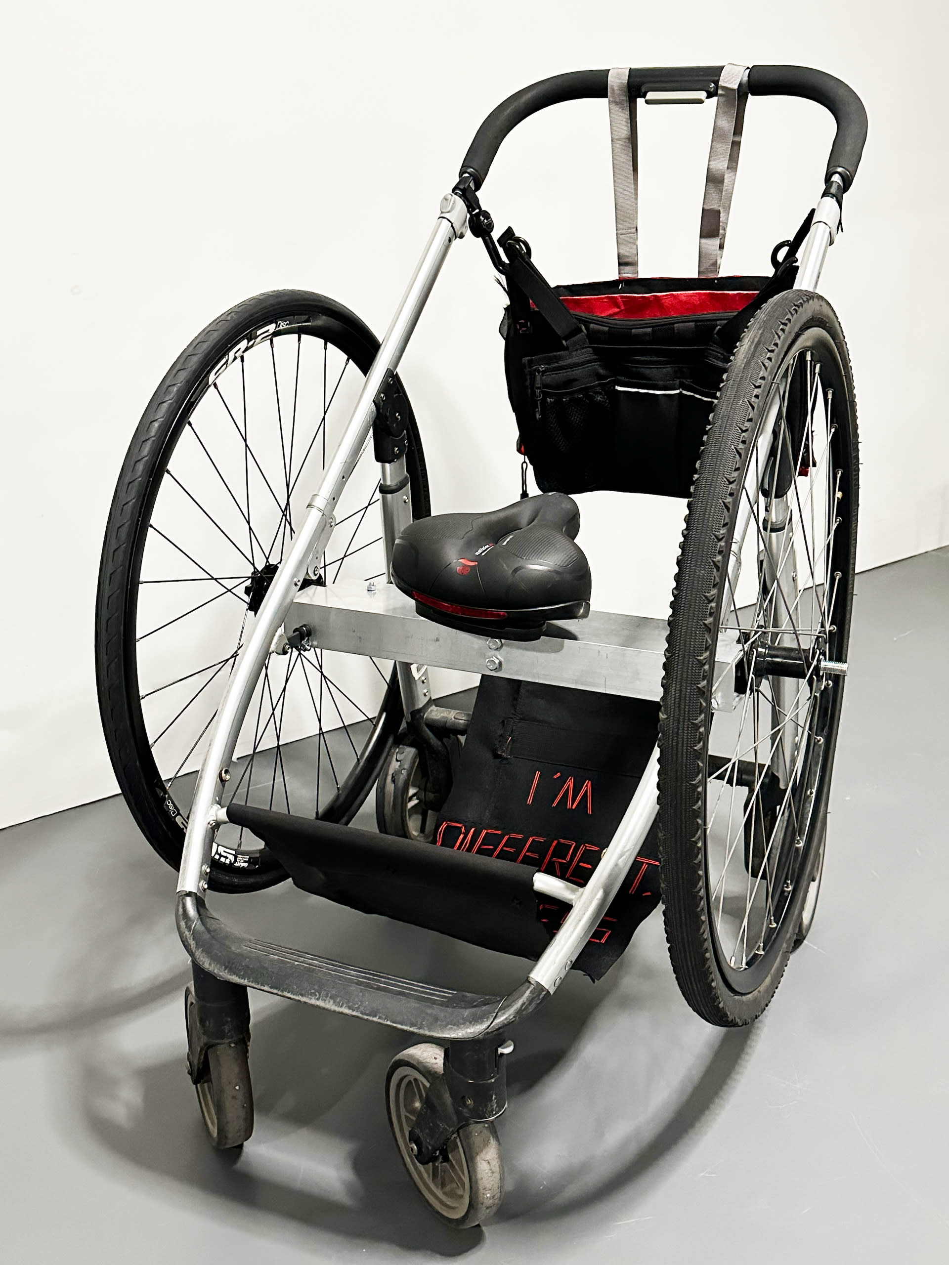 front view of the object, showing the bike seat as well as the fabric with the texts: "I'm different, not less"