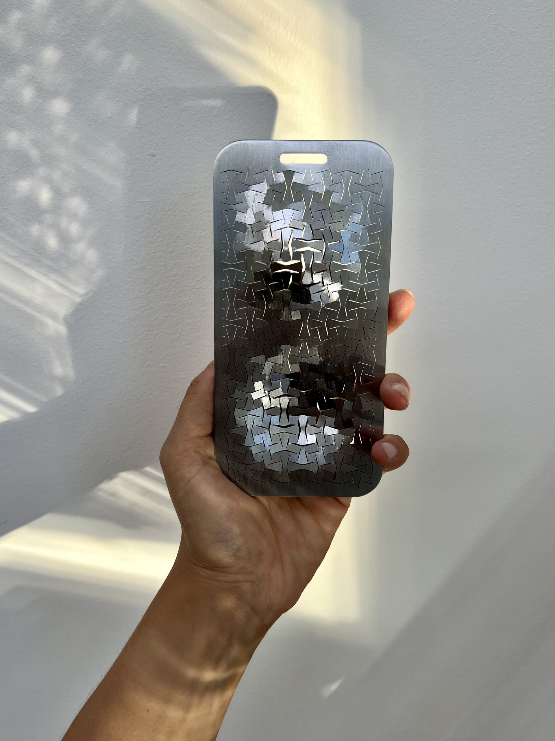 Steel phone object with lines cut through it and held up with a hand