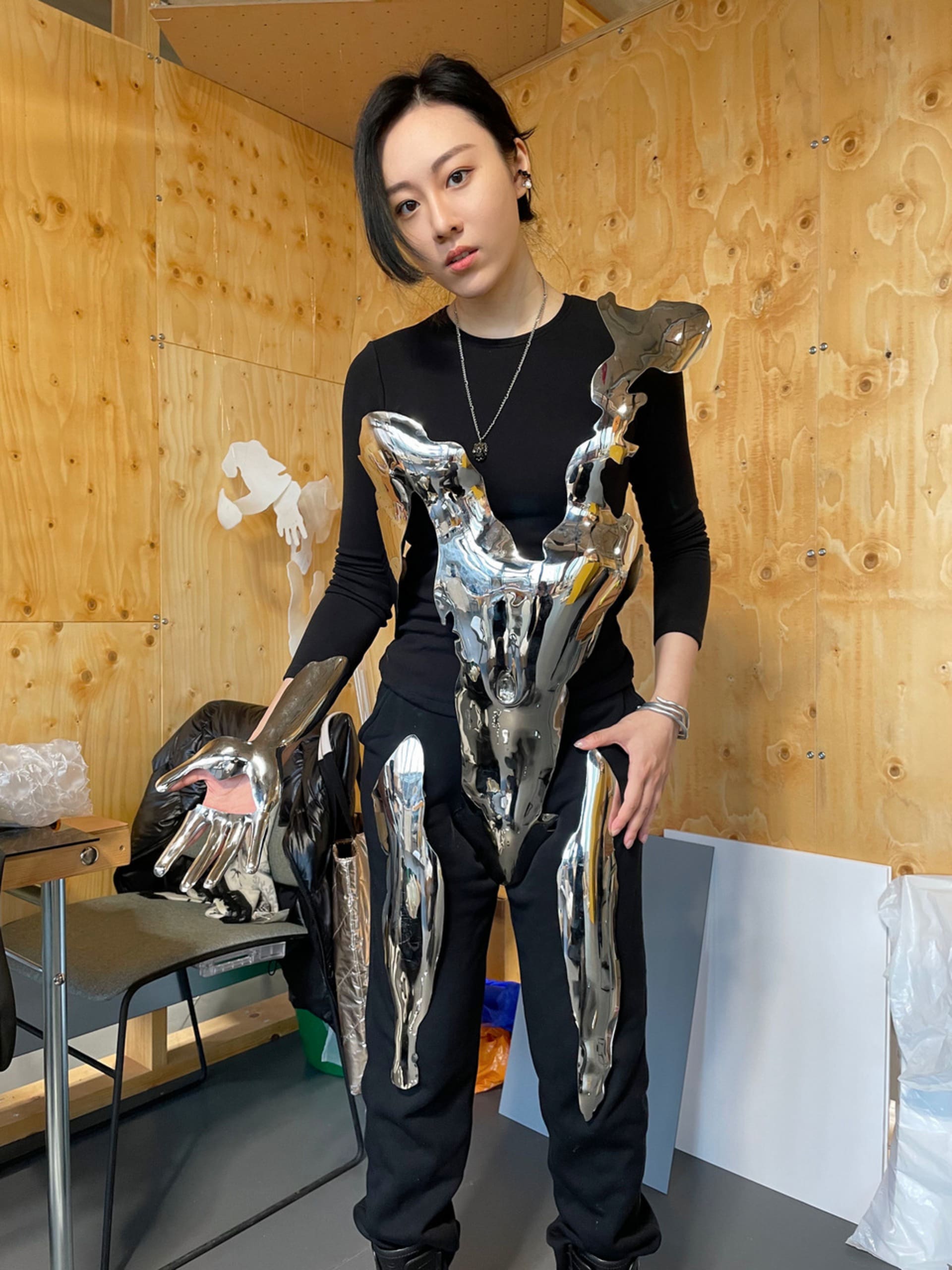 Portrait of the artist standing in black, wearing one of her stainless steel body works.