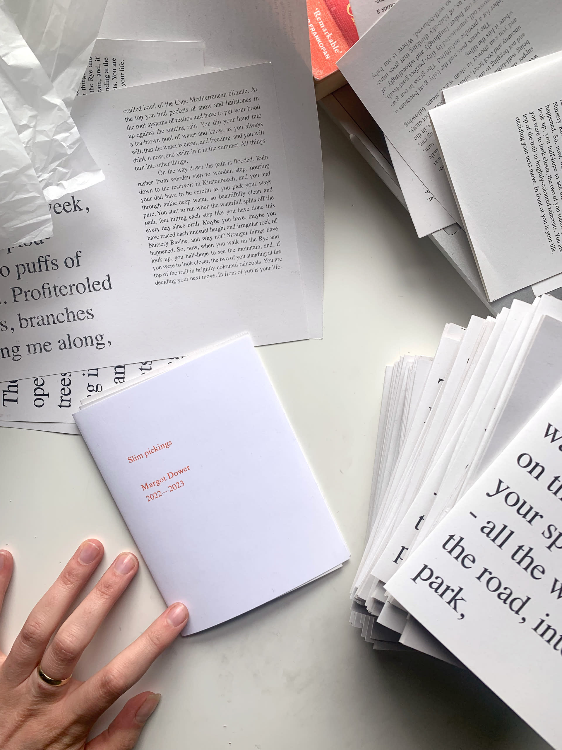 An image of a desk with papers scattered on it. A hand is resting on one of the pages.