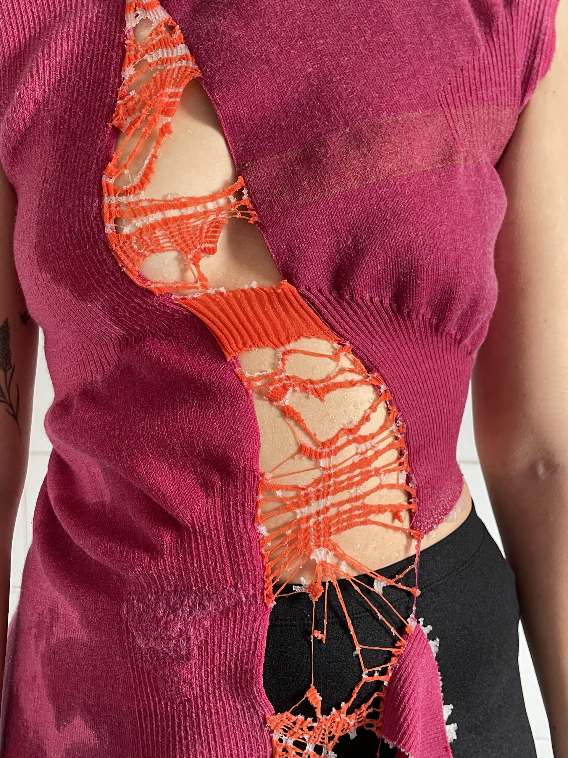 Close up photo of a pink knitted garment with orange centre panel that has been dissolved.