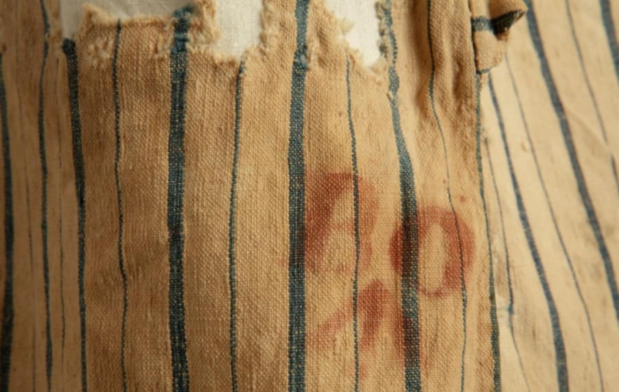 A close-up photo of a white shirt with blue stripes, showing a red 'BO' stamp with a broad arrow marking