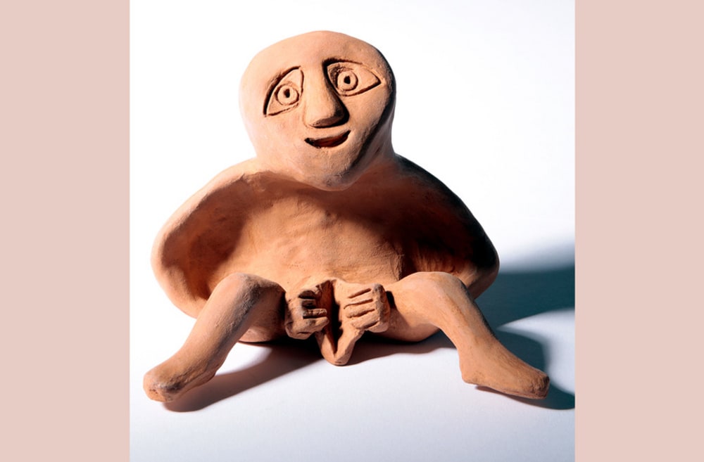 A terracotta Sheela-na-gig sits with her legs apart and her vulva splayed - she is a symbol of fertility 