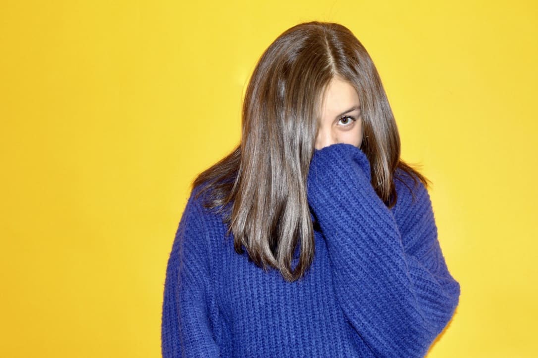 A woman with a blue sweater on a bright yellow background.